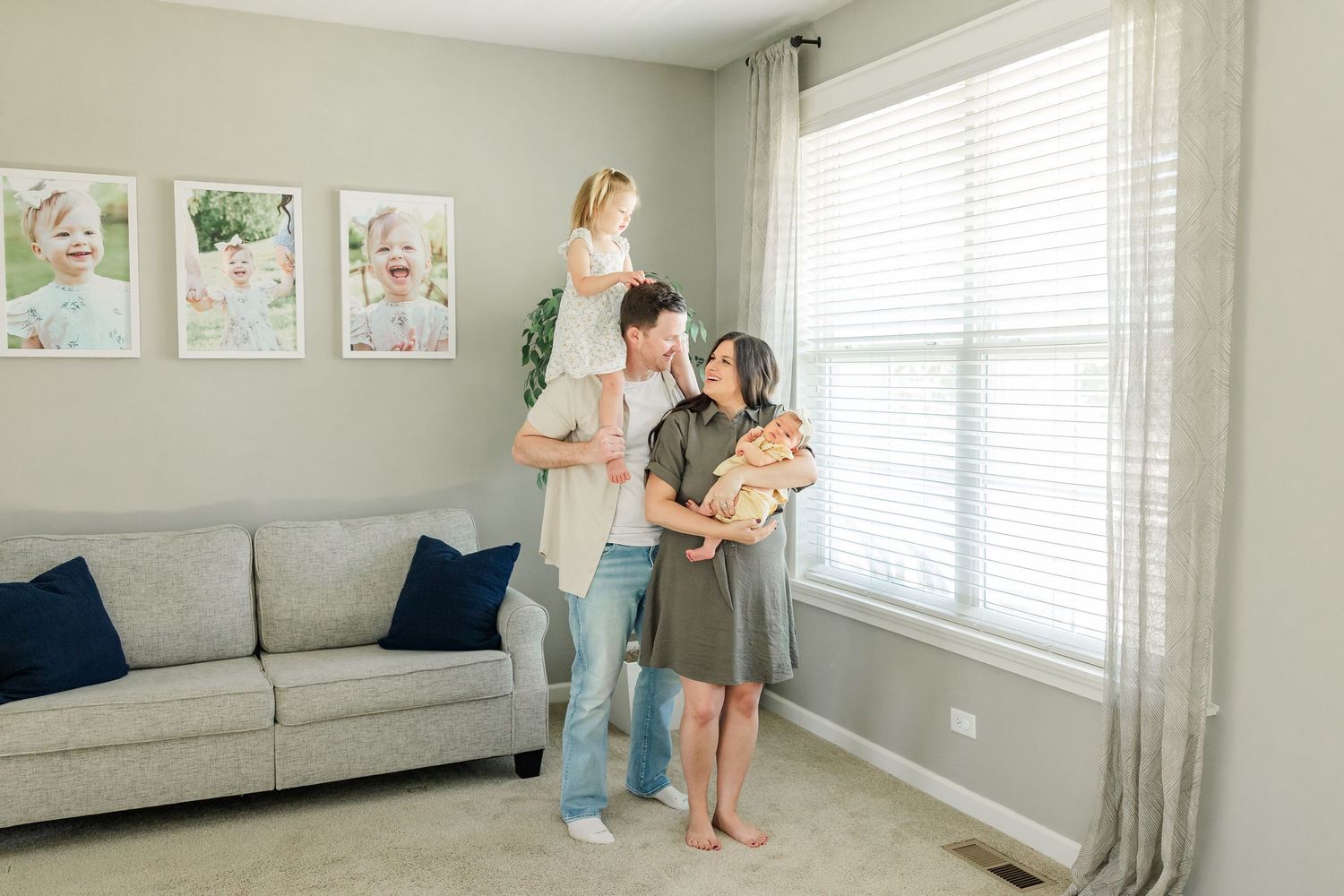 Bright in-home newborn session with parents, big sister, and baby girl standing together by the window