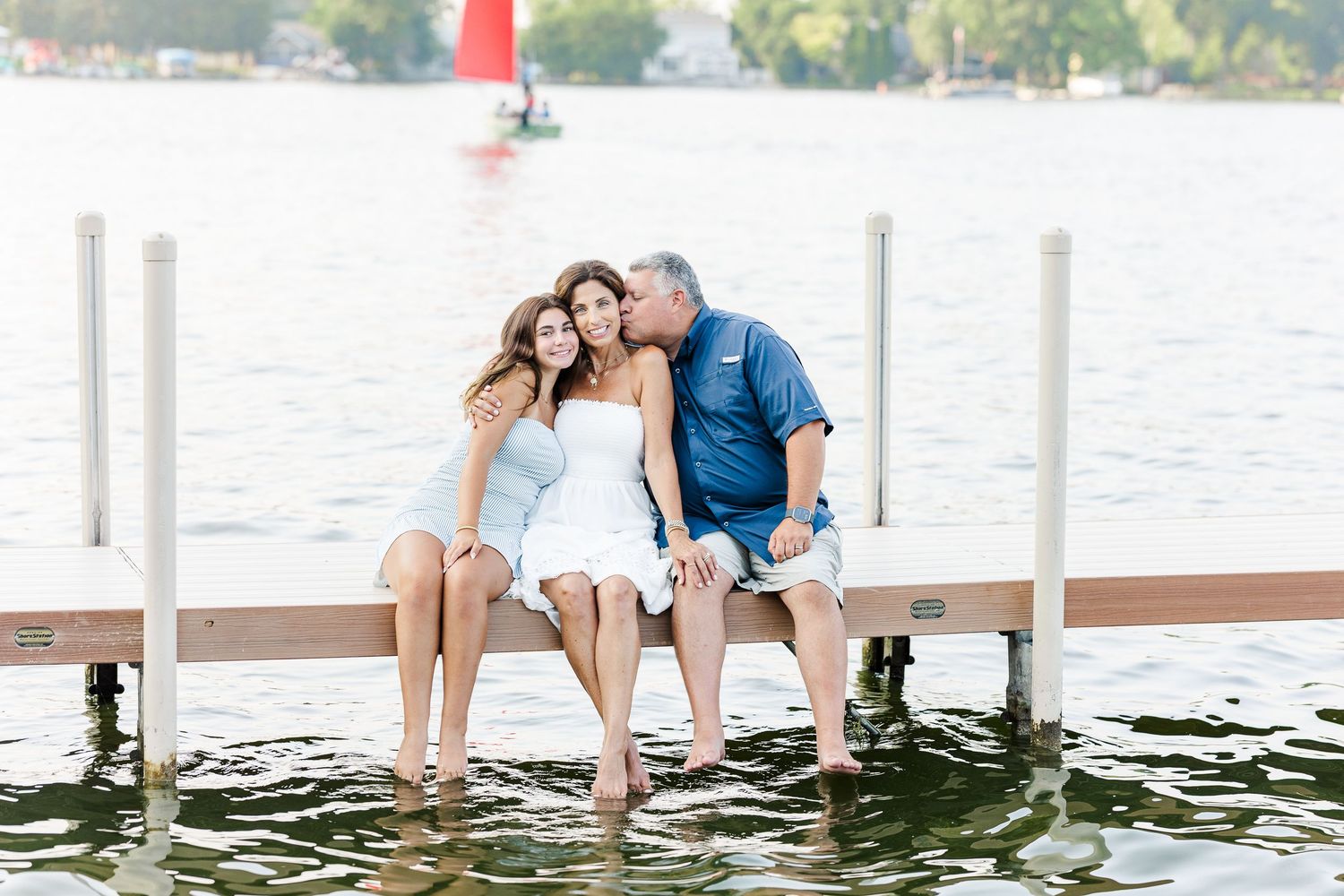 Family sitting on dock during Pistakee Lake family photos with sailboat in background