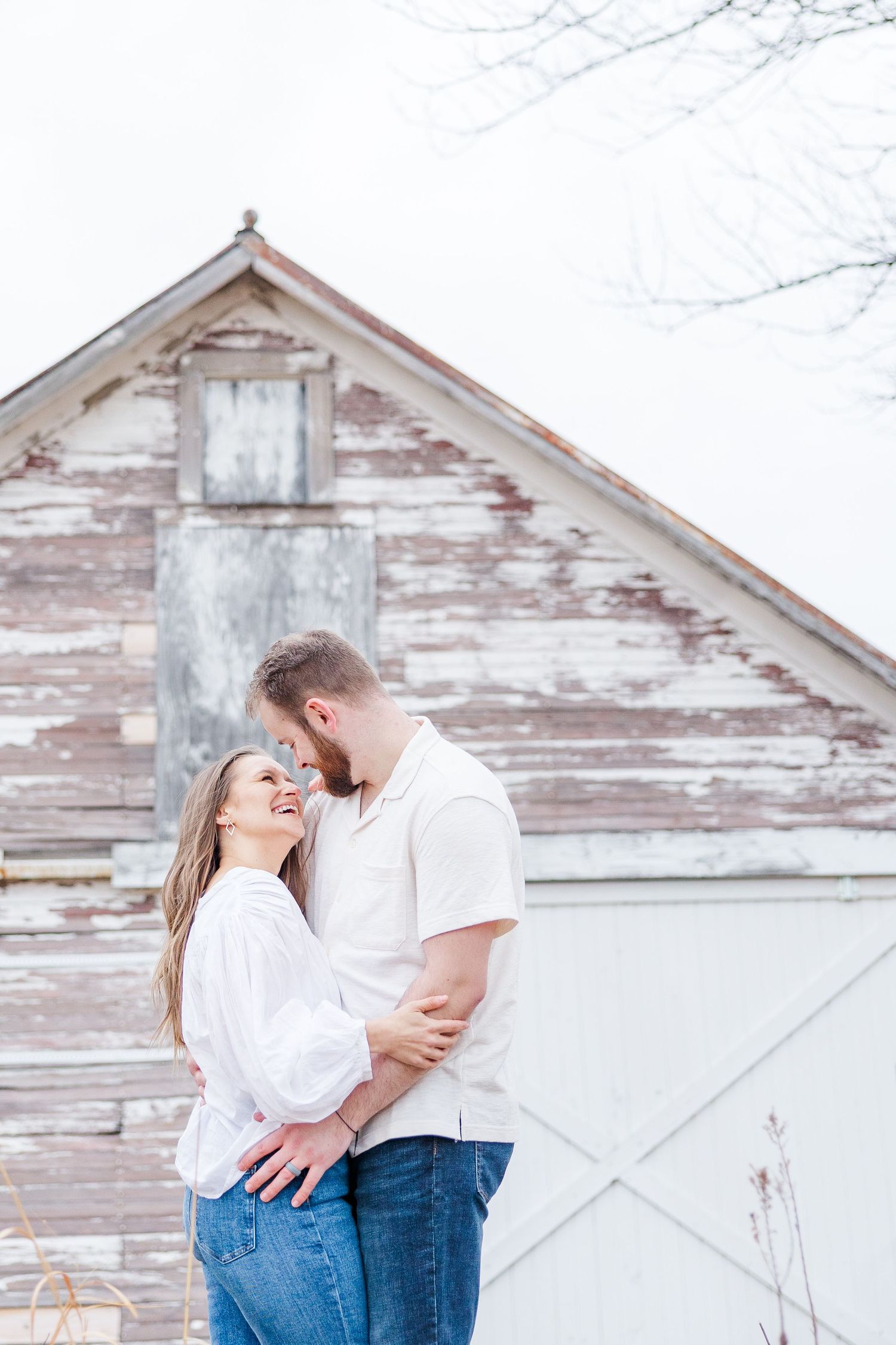Couple embracing by rustic barn during pregnancy announcement photos in Cary, Illinois