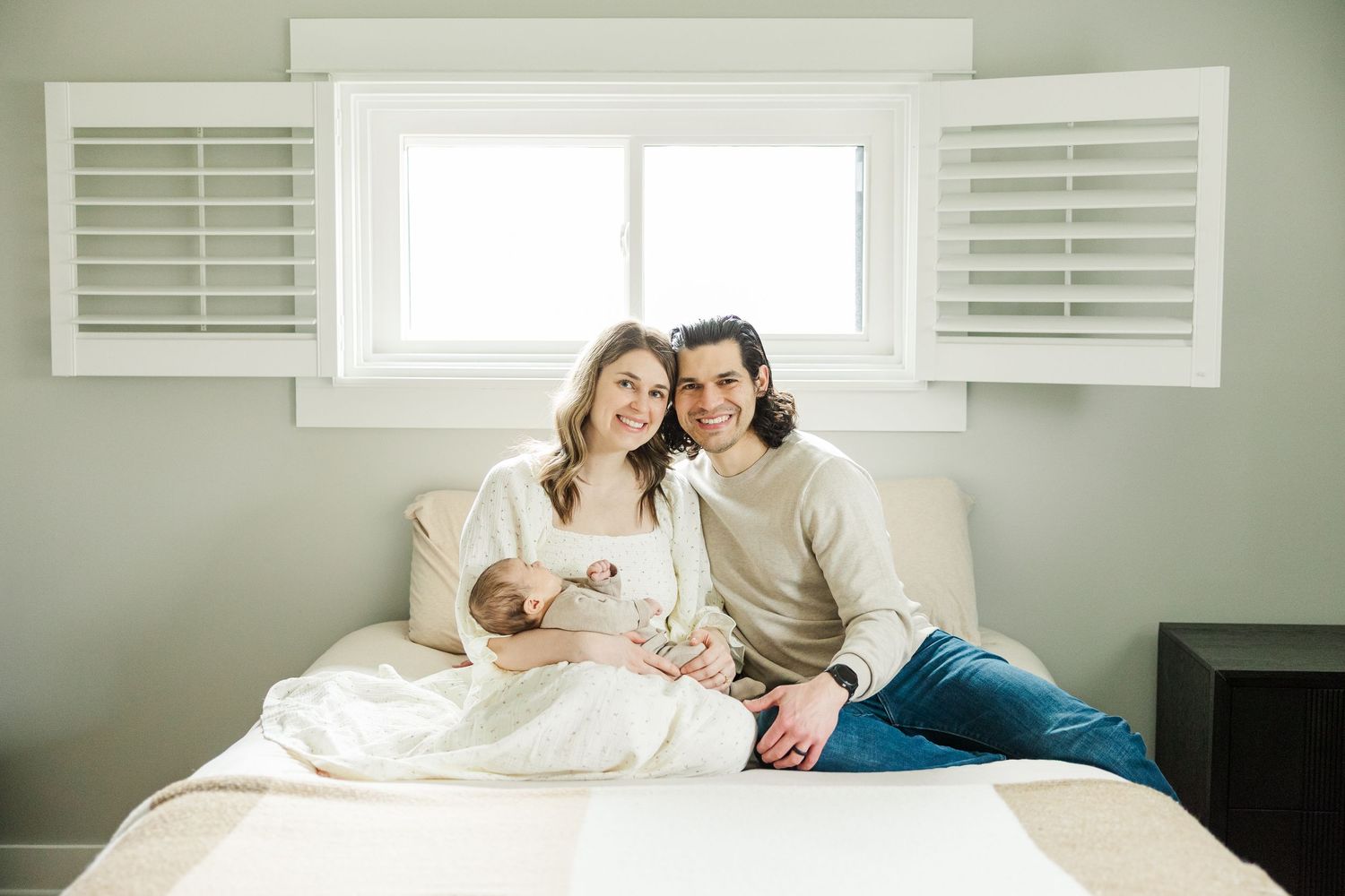 Parents sitting on their bed holding their newborn baby during an in-home lifestyle newborn session in Palatine Illinois