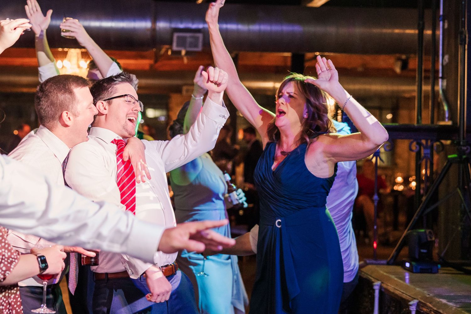 Wedding guests dance enthusiastically with raised arms on a festive dance floor.