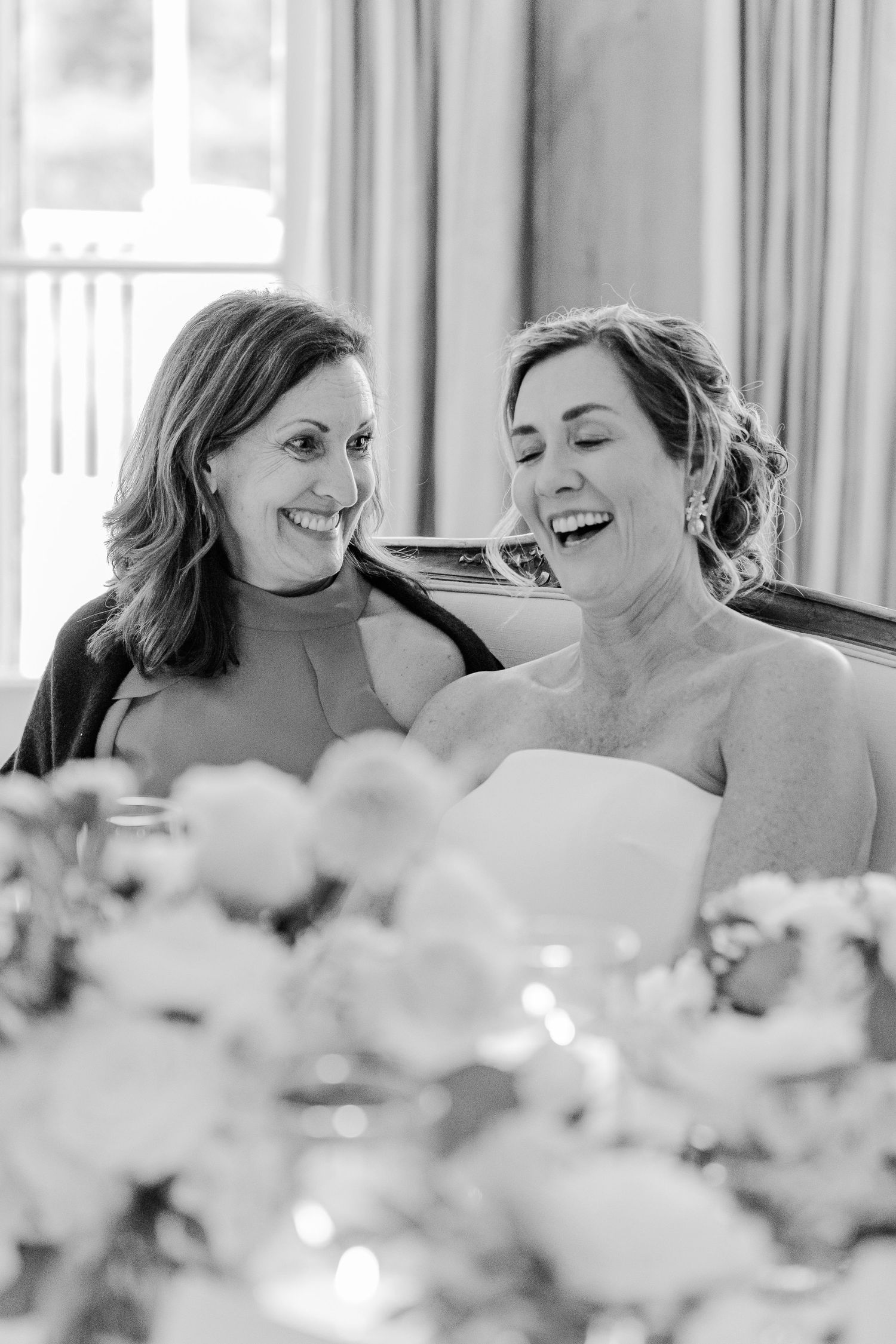 Black and white candid moment of shared joy between two women at formal event.