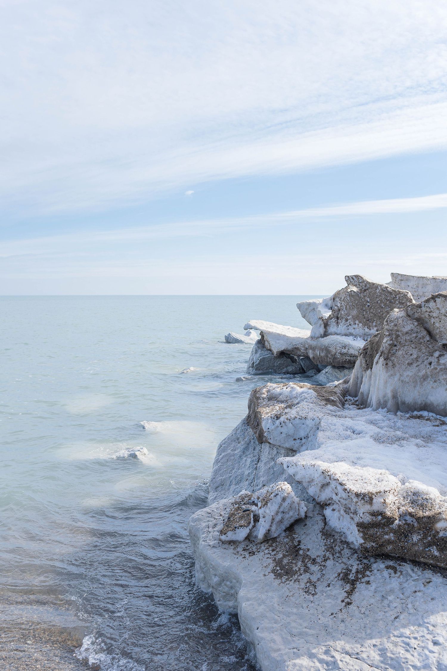 Ice-covered limestone cliffs along a frozen lake shoreline under cloudy skies.