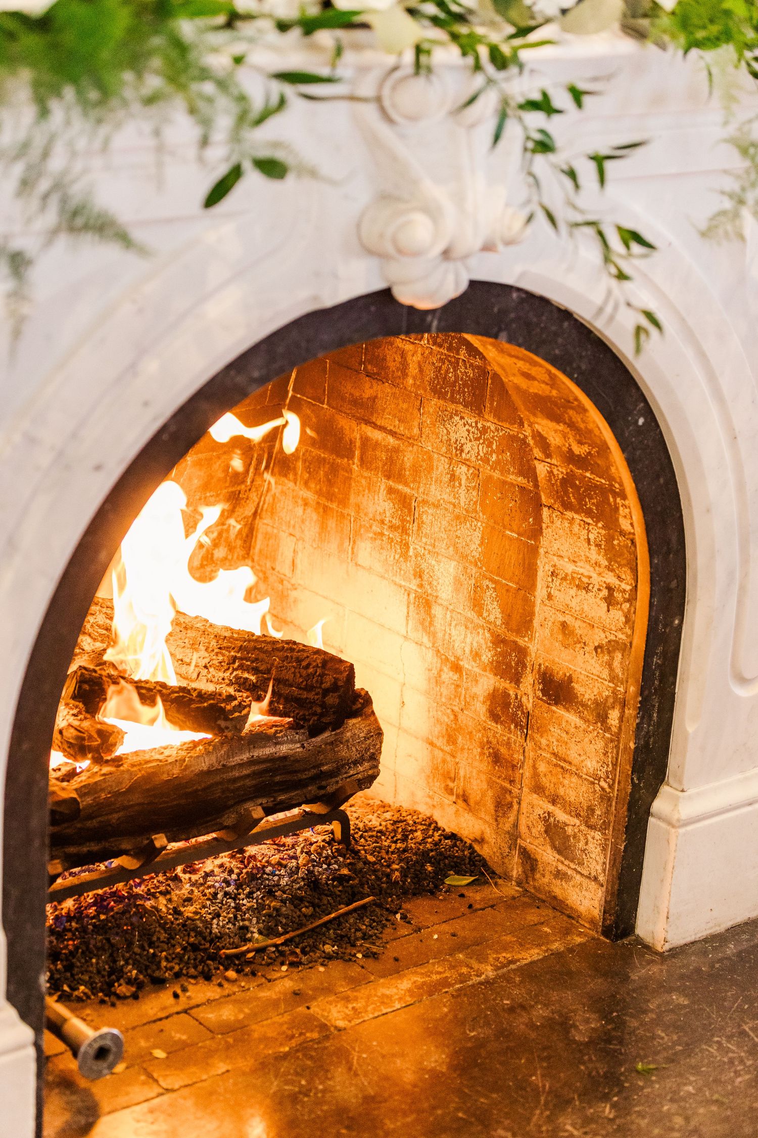 Cozy lit fireplace with burning logs inside decorative white marble or stone surround.