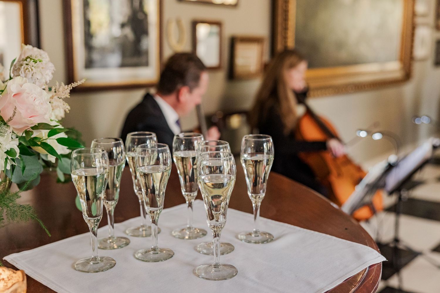 Champagne flutes arranged on white tablecloth with cellist performing in background.