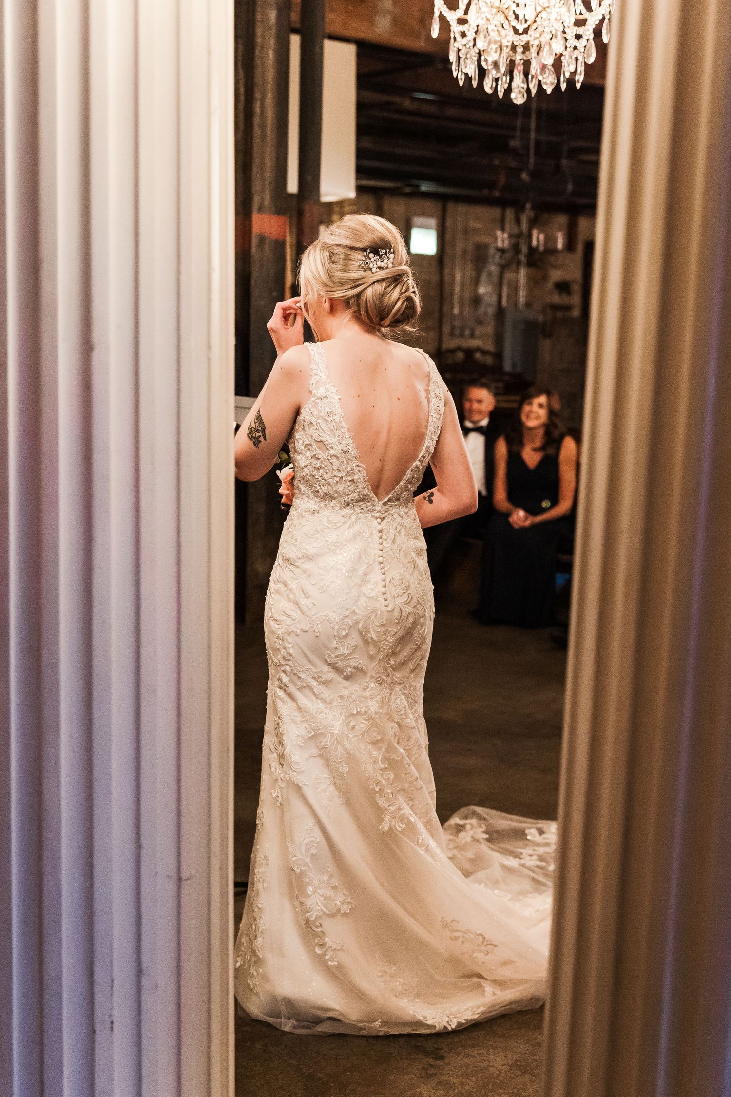 Back view of bride in lace wedding dress with crystal chandelier overhead.