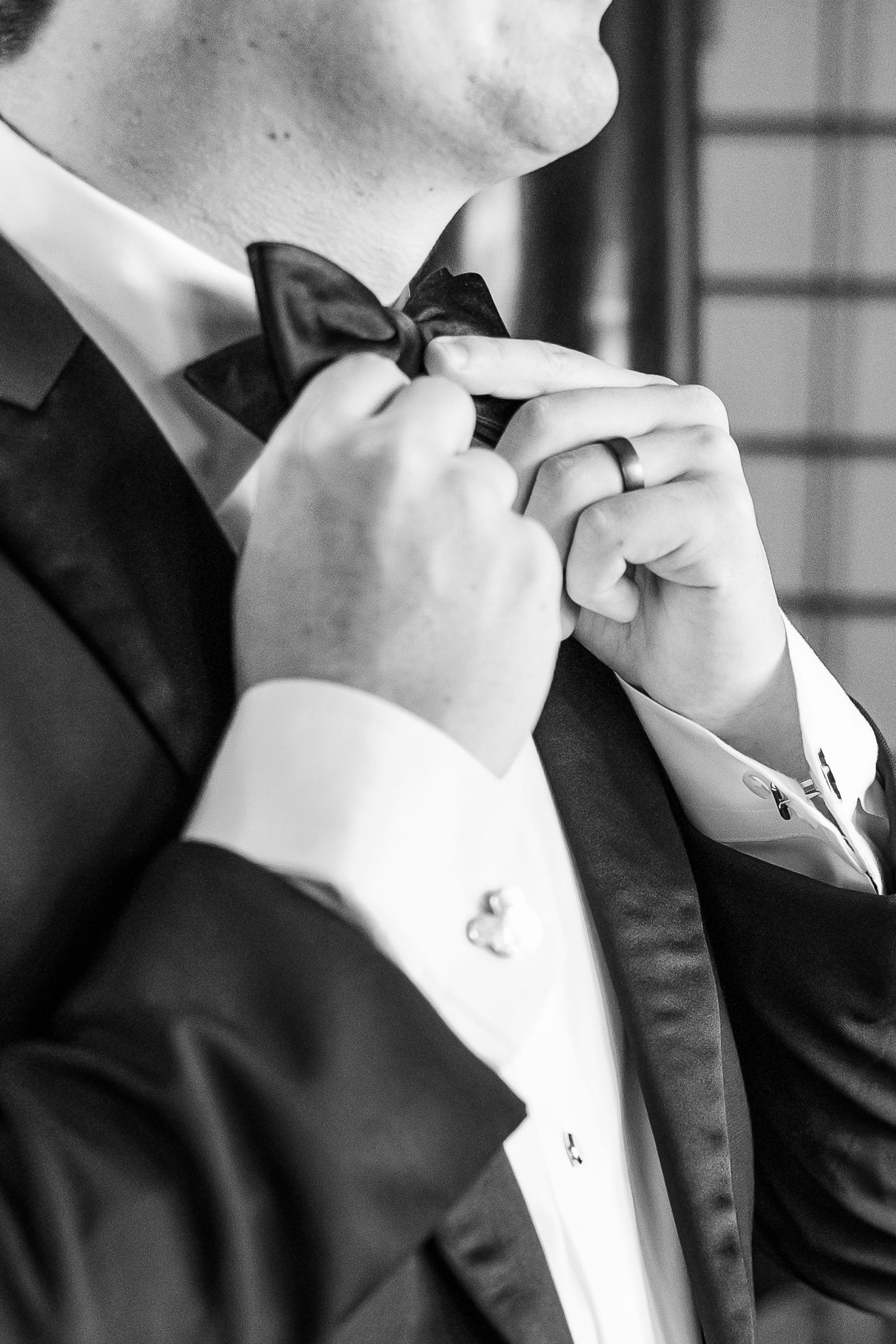 Close-up black and white image of hands adjusting a bow tie.