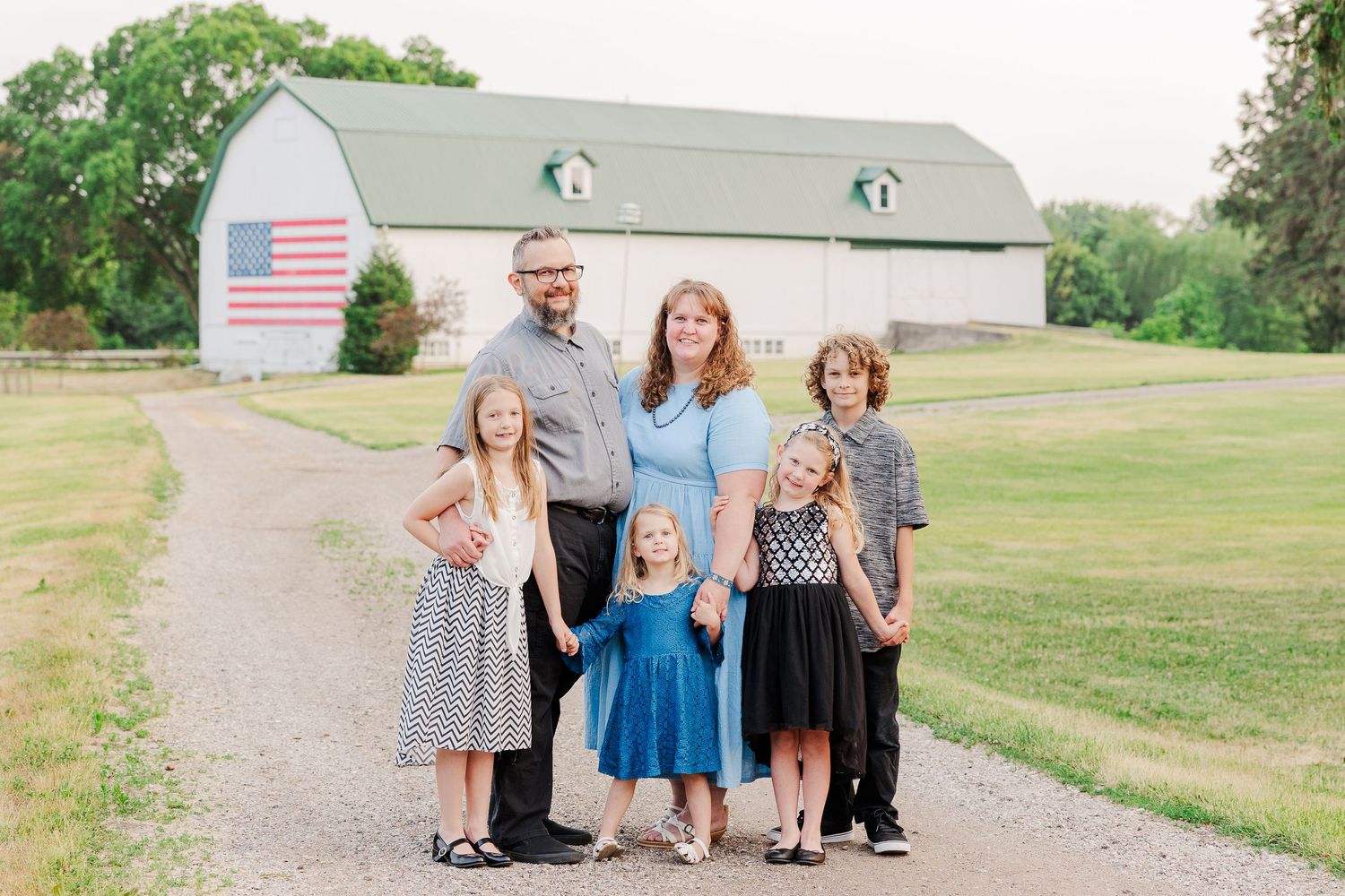 Group photo in front of a rustic barn with American flag showing casual coordinated outfits.