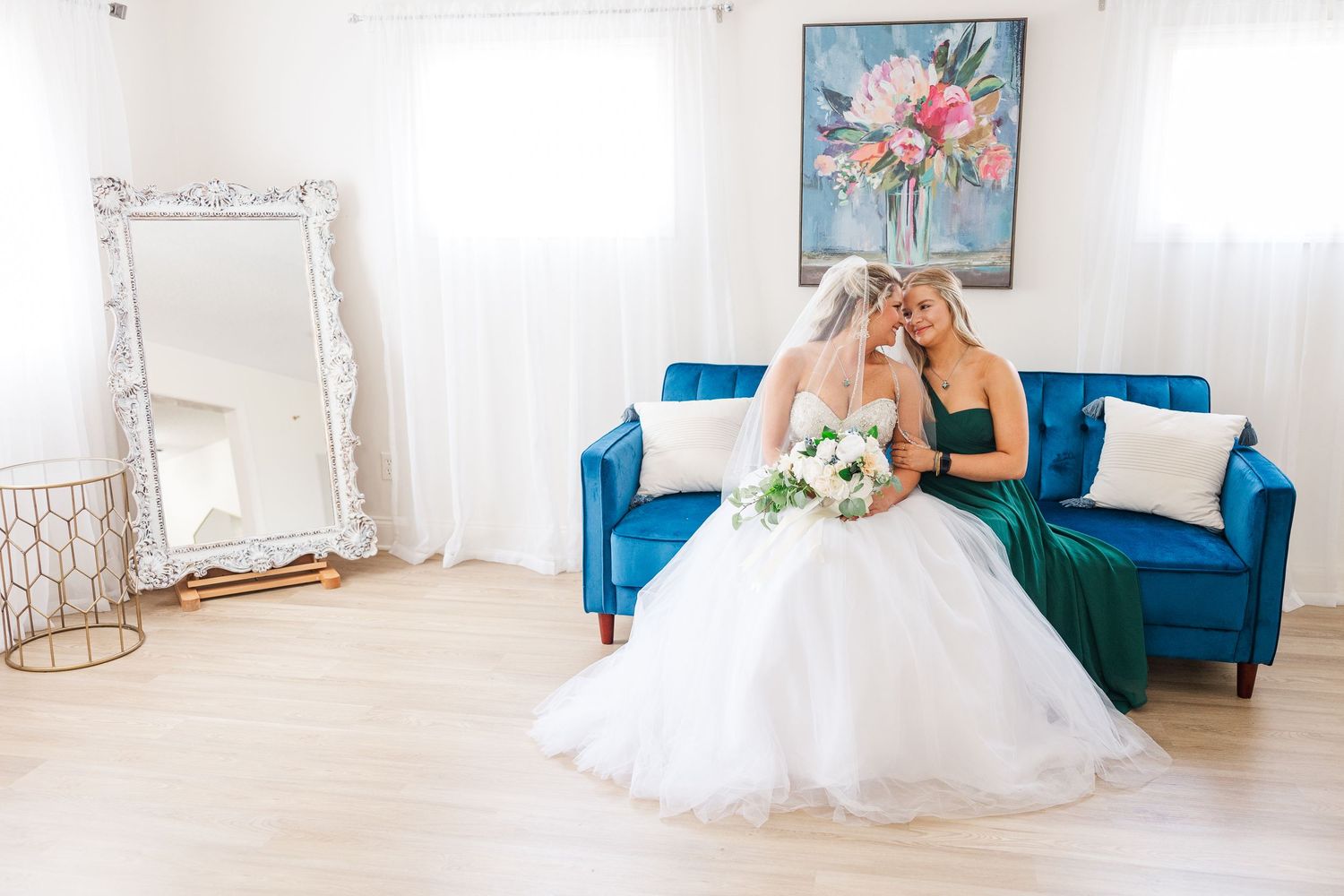 Wedding scene with bright blue velvet couch and floral wall art in a white studio setting.