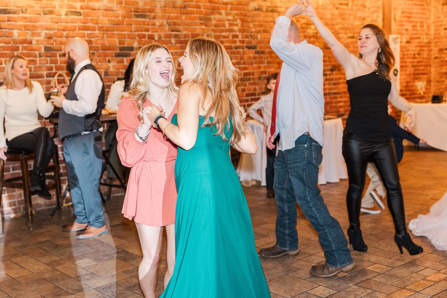 Wedding guests dancing and celebrating in colorful dresses at a rustic reception venue.