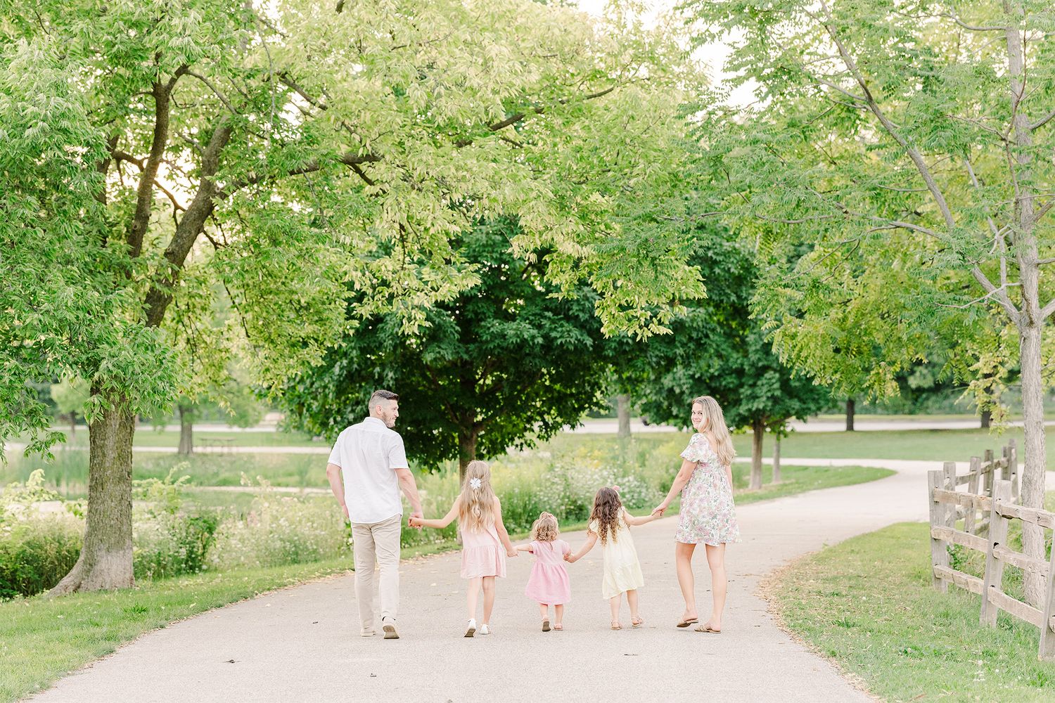 Family walking together hand in hand down rural path surrounded by green trees.