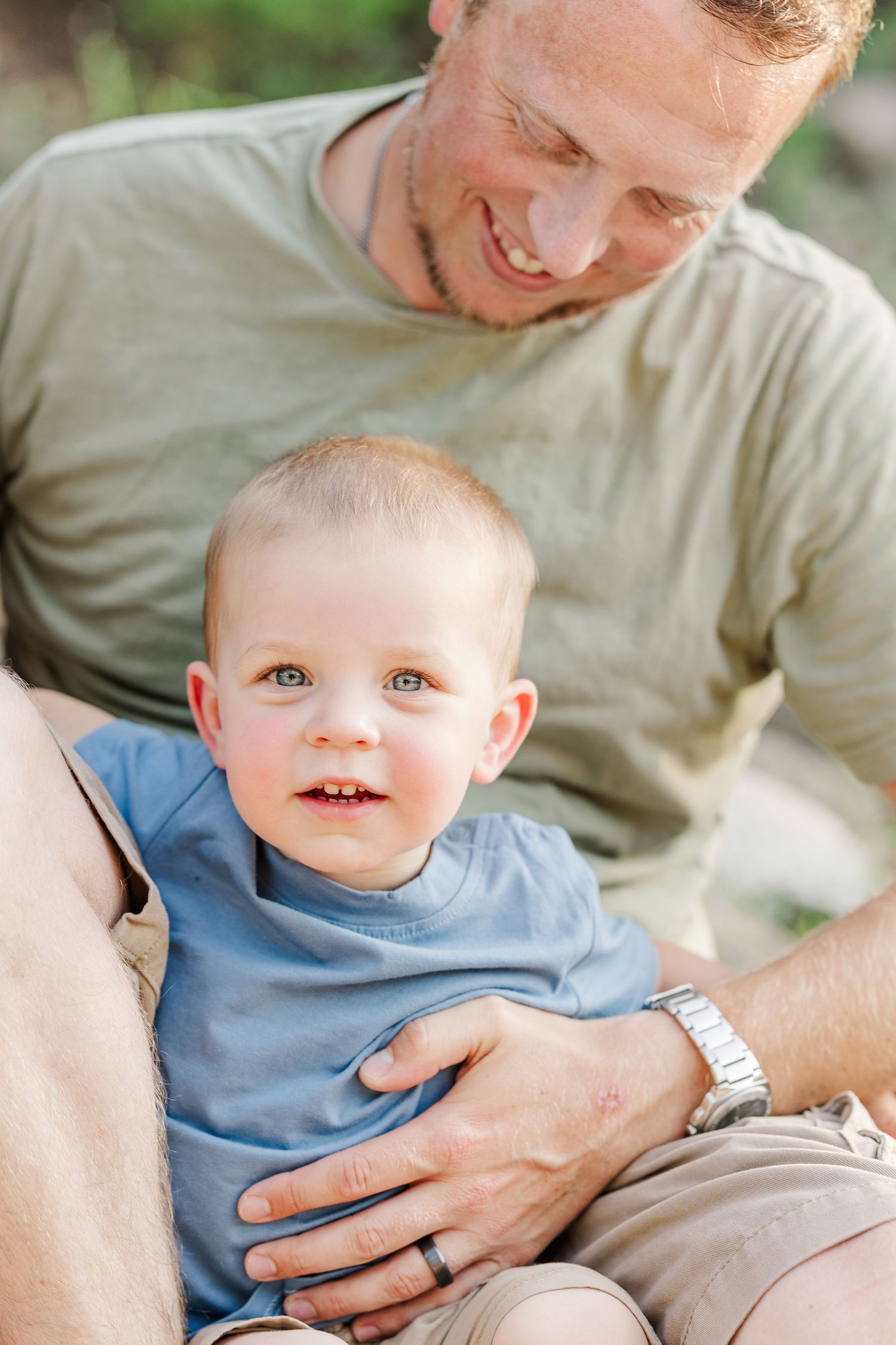 A young child in a blue shirt sits on a lap during a tender outdoor portrait.