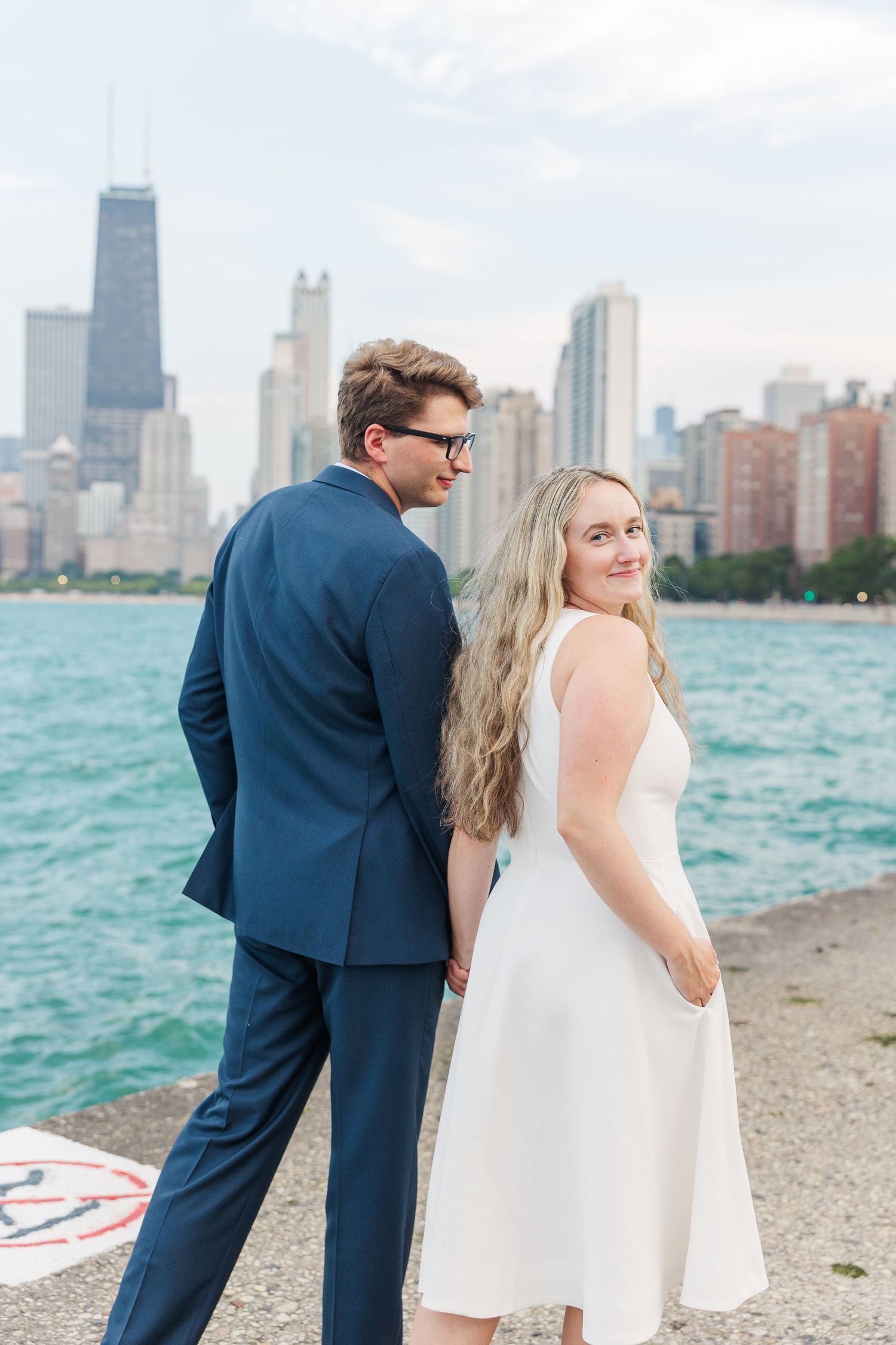 Elizabeth and Joe holding hands with the Chicago skyline in the background at North Avenue Beach during sunset