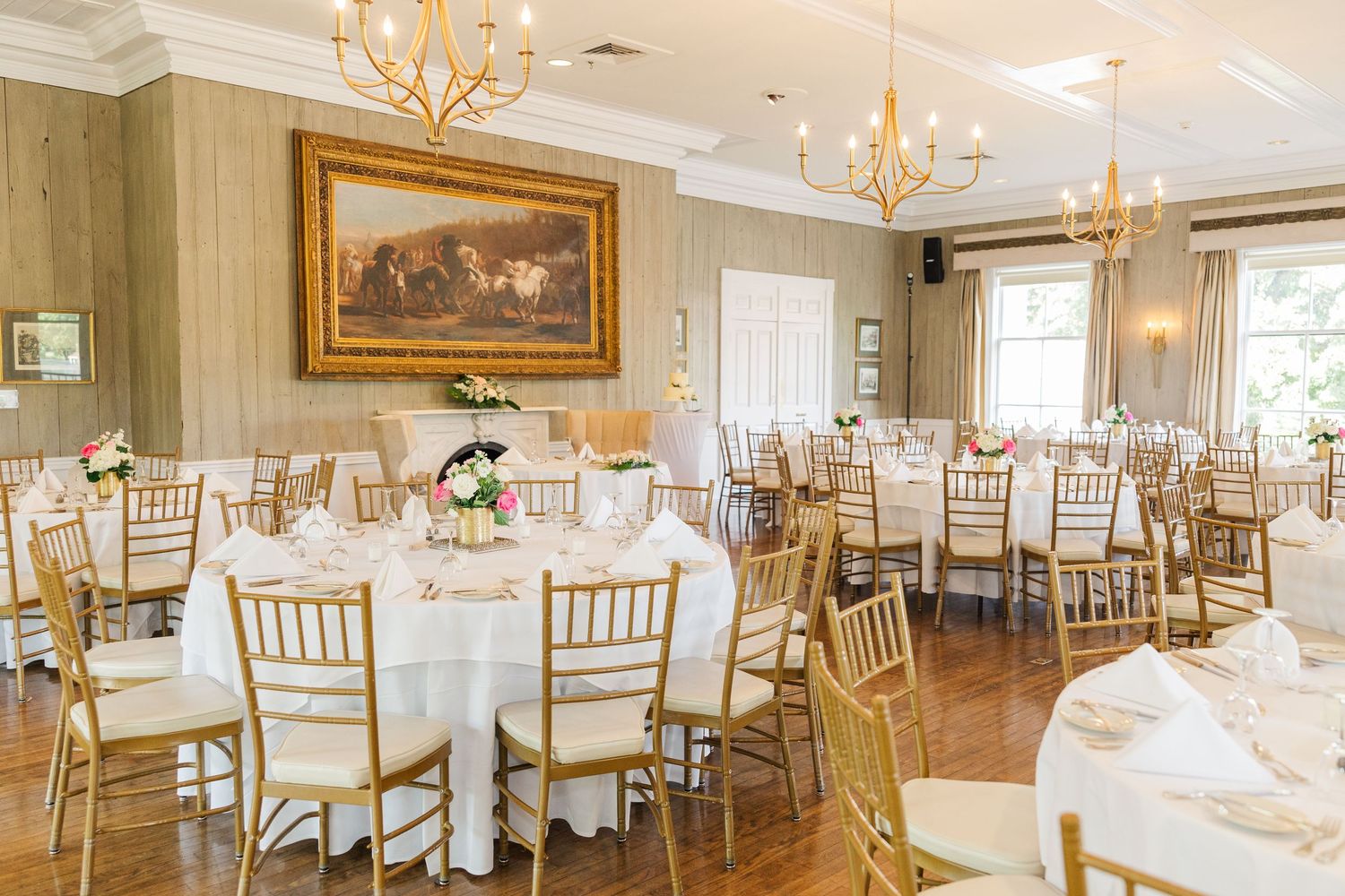 Elegant wedding reception venue with round tables, gold chiavari chairs, and crystal chandeliers.