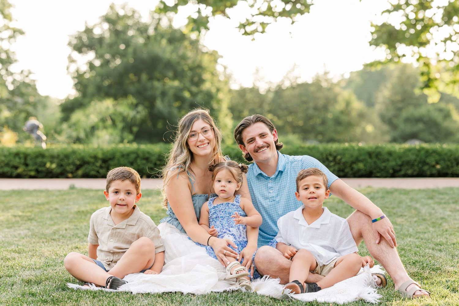 Smiling family of five relaxing on white blanket in green park on a bright sunny day.