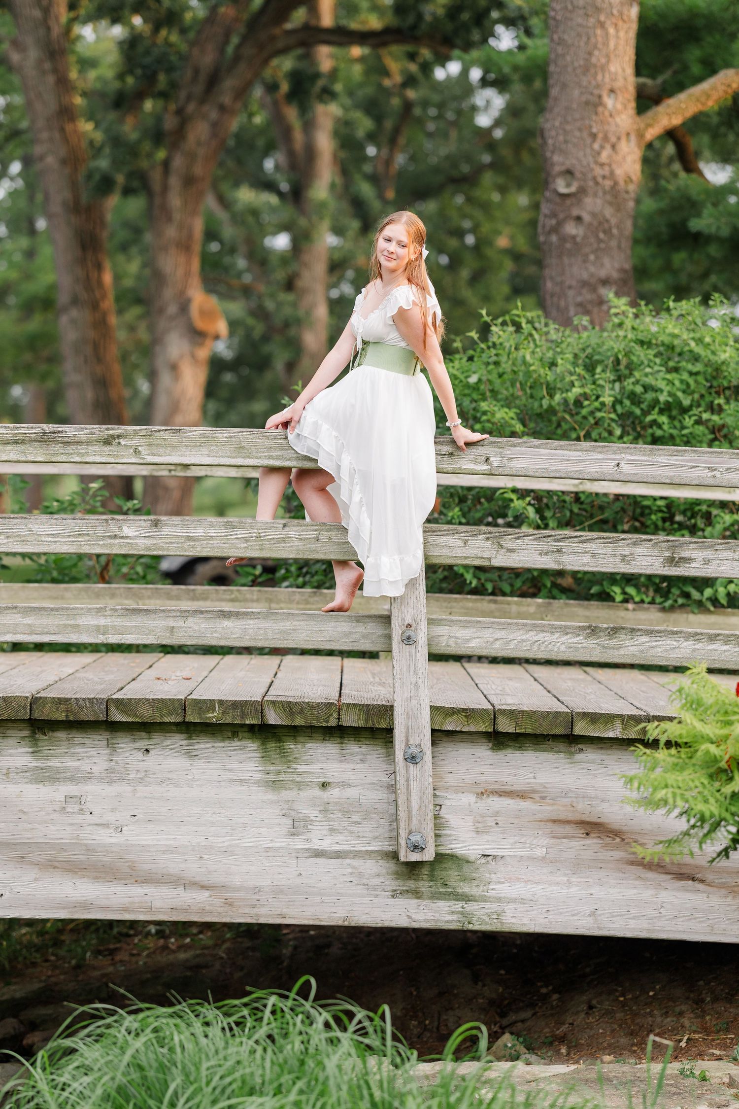 Samantha poses barefoot on a rustic wooden bridge during her whimsical senior portrait session.