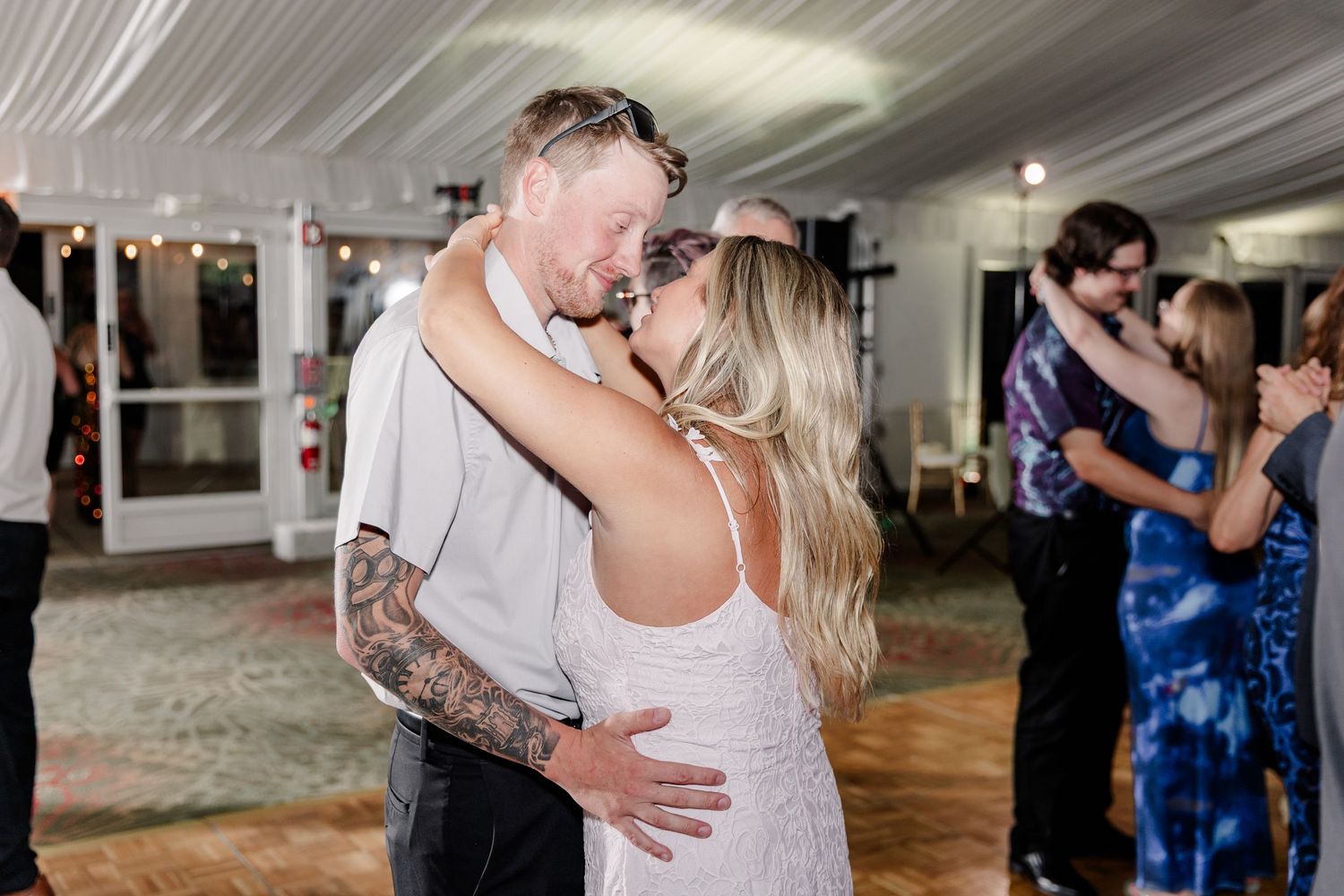Couple sharing intimate slow dance embrace at warmly lit wedding reception dance floor.