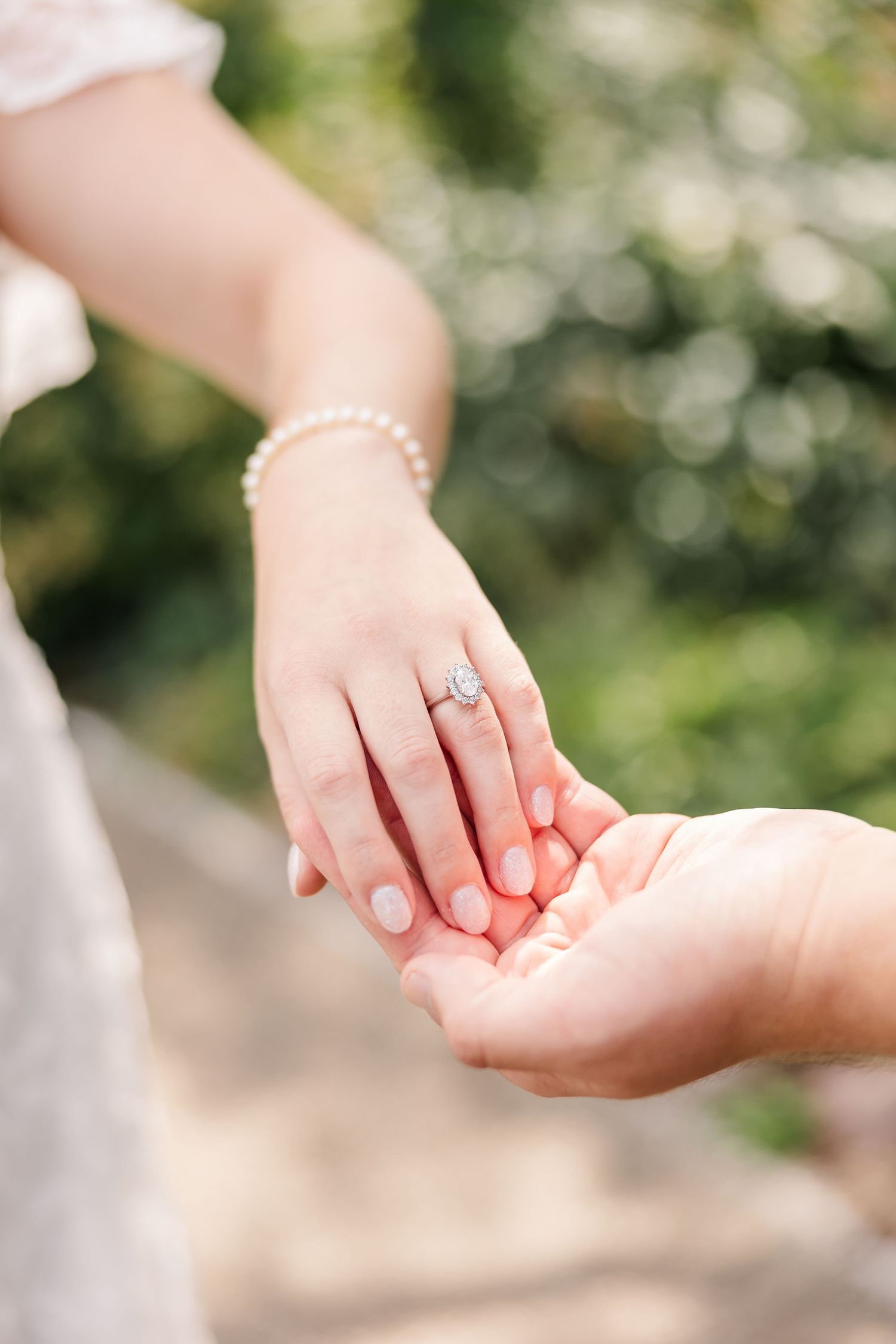 Close-up of bride's hand displaying diamond engagement ring with pearl bracelet held by groom.