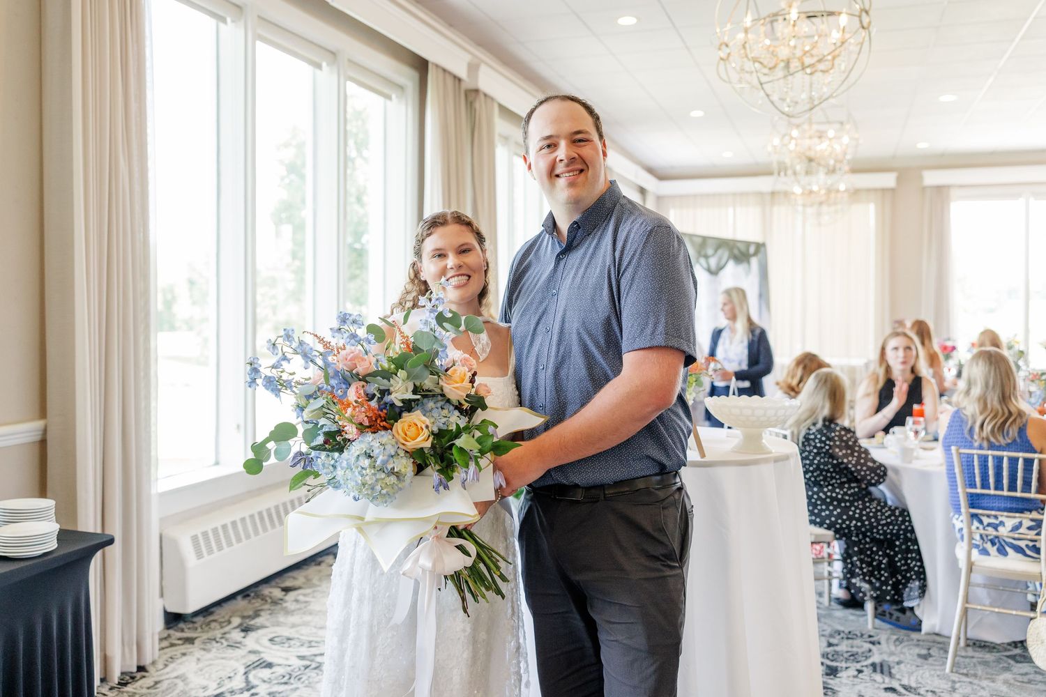 Smiling couple posing with a colorful floral bouquet at an elegant wedding reception venue.