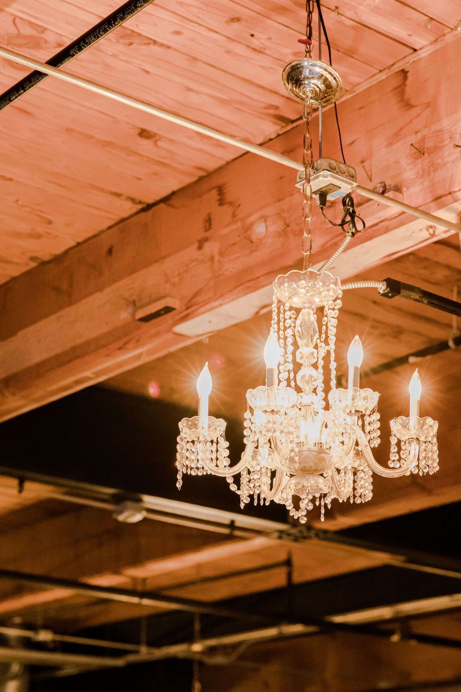 Elegant crystal chandelier illuminates a rustic wooden ceiling in warm light.