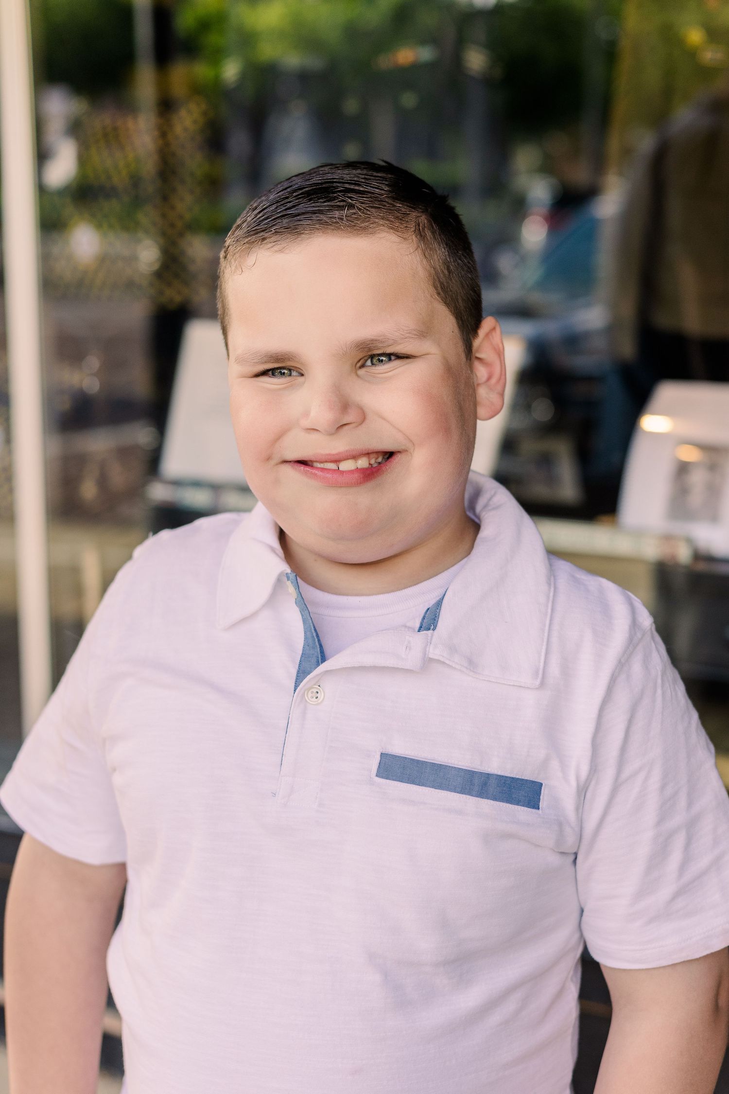 Portrait of youth in white polo shirt smiling warmly at camera outdoors.