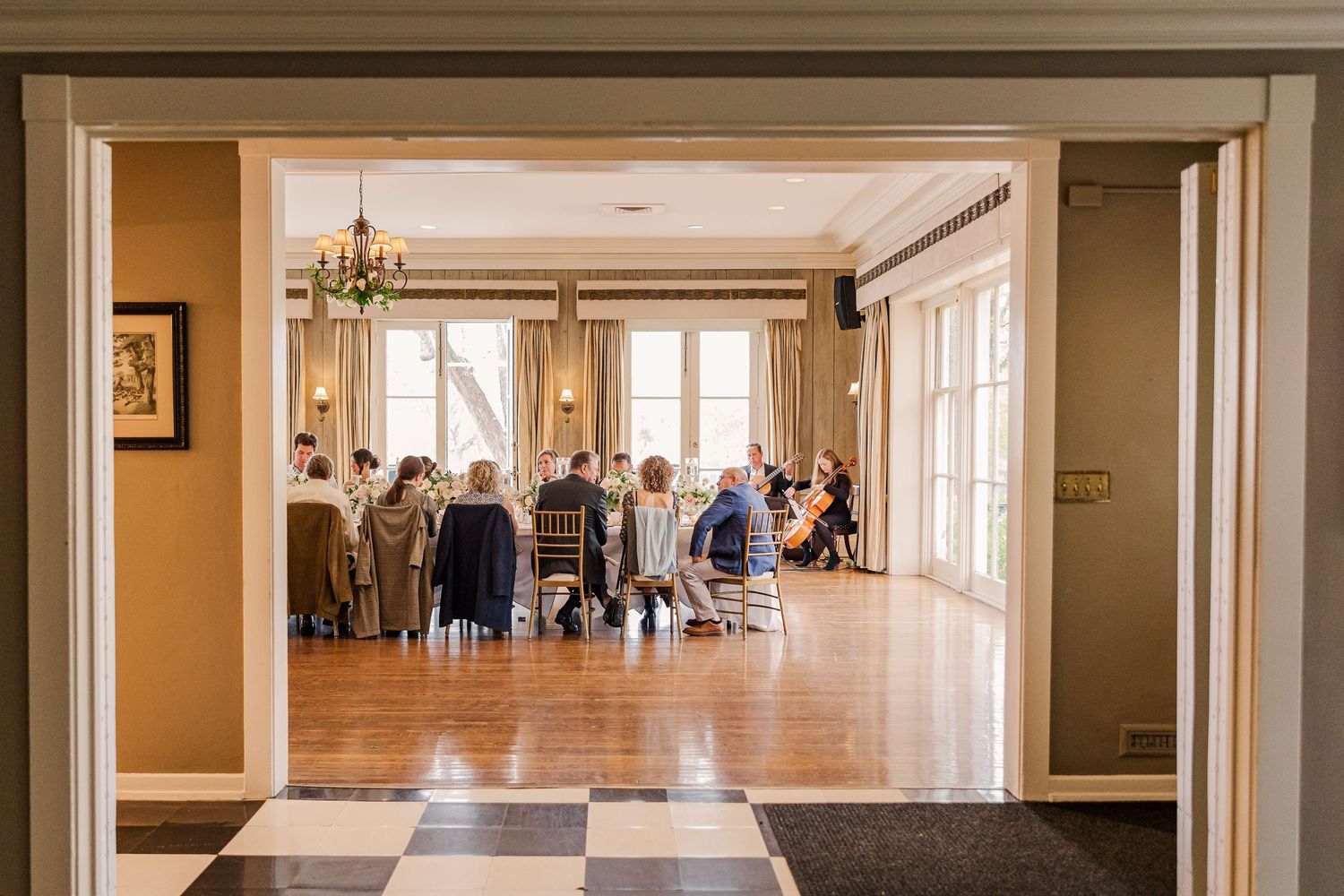 Elegant reception hall viewed through doorway with dining tables and guests gathering.