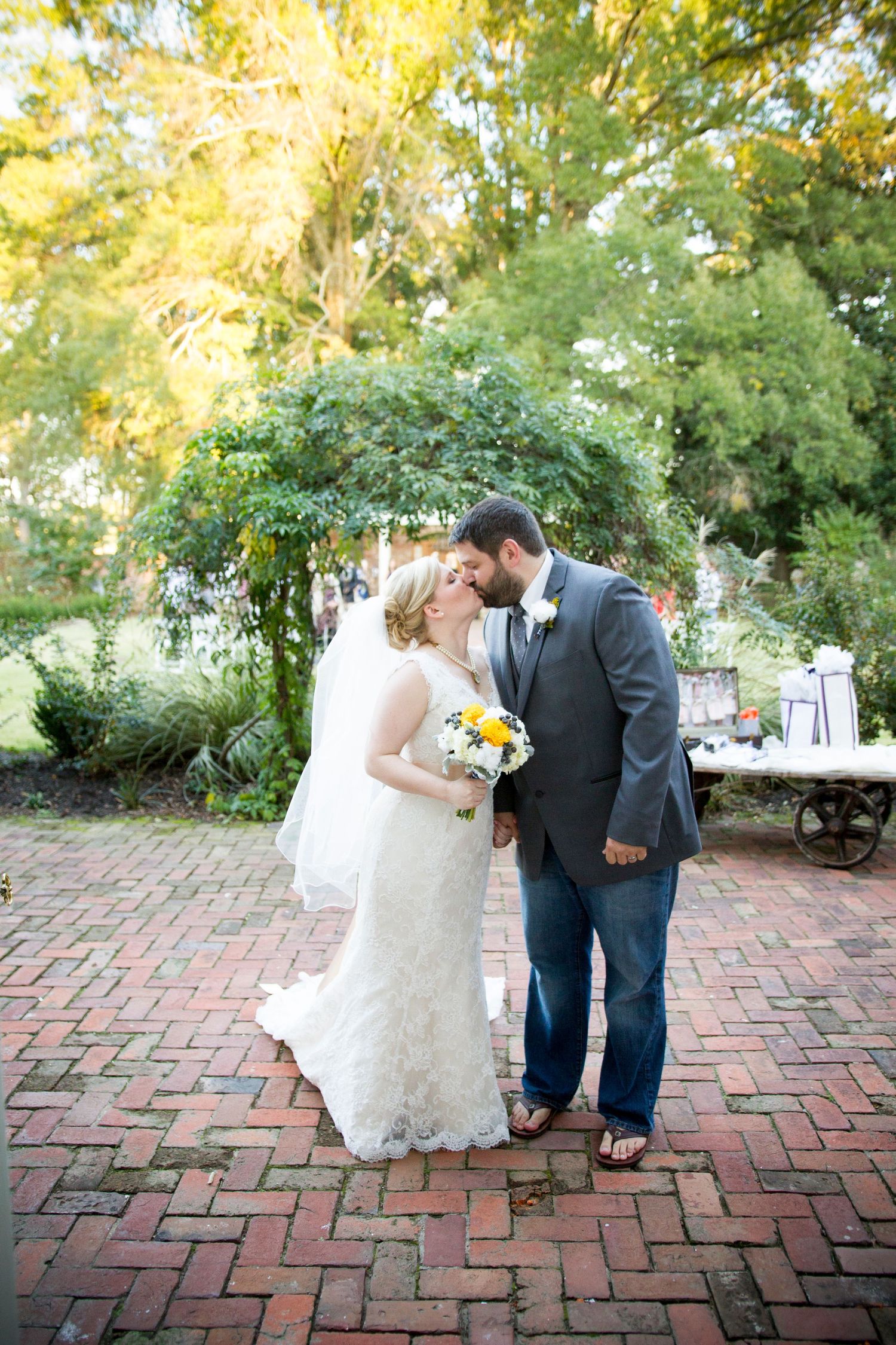 Romantic wedding portrait in a garden setting with brick pathways and natural greenery.