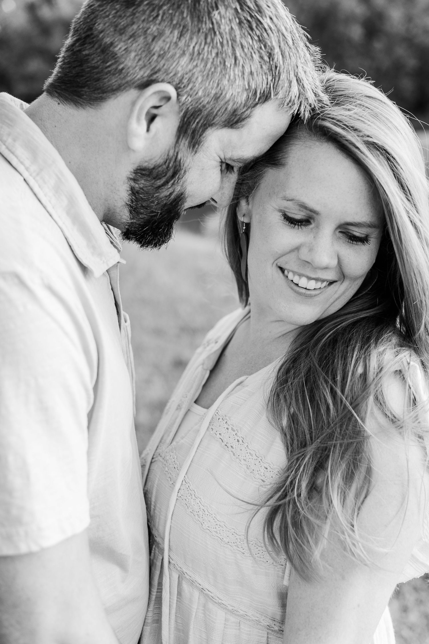 A black and white photograph captures a tender moment between a couple outdoors.