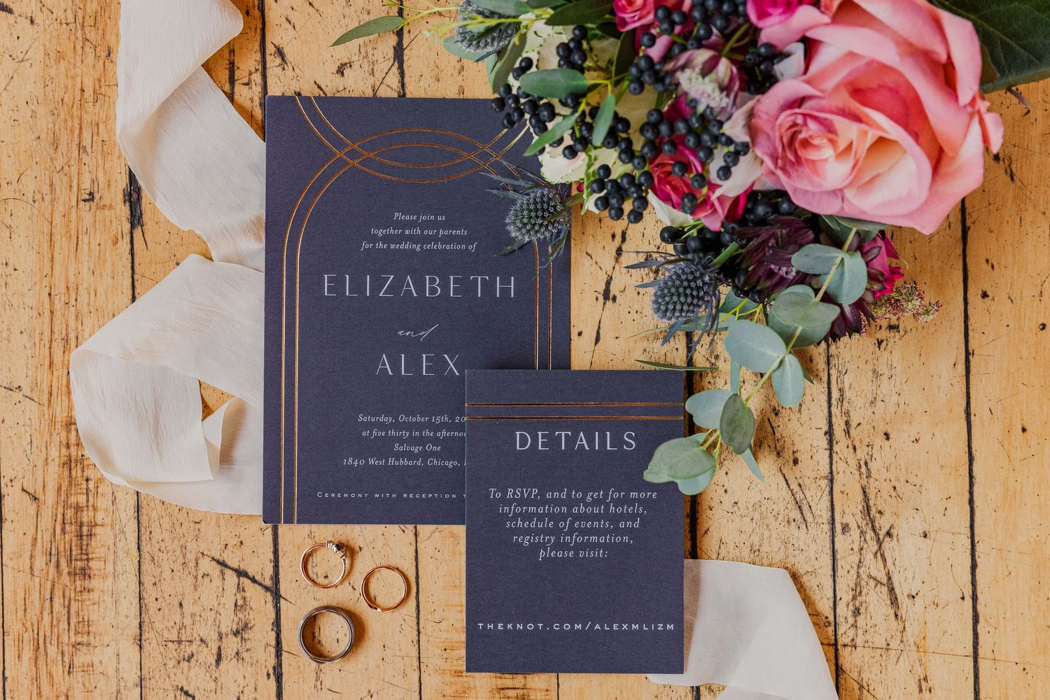 Elegant navy and copper wedding invitation suite with rings and pink floral arrangements.