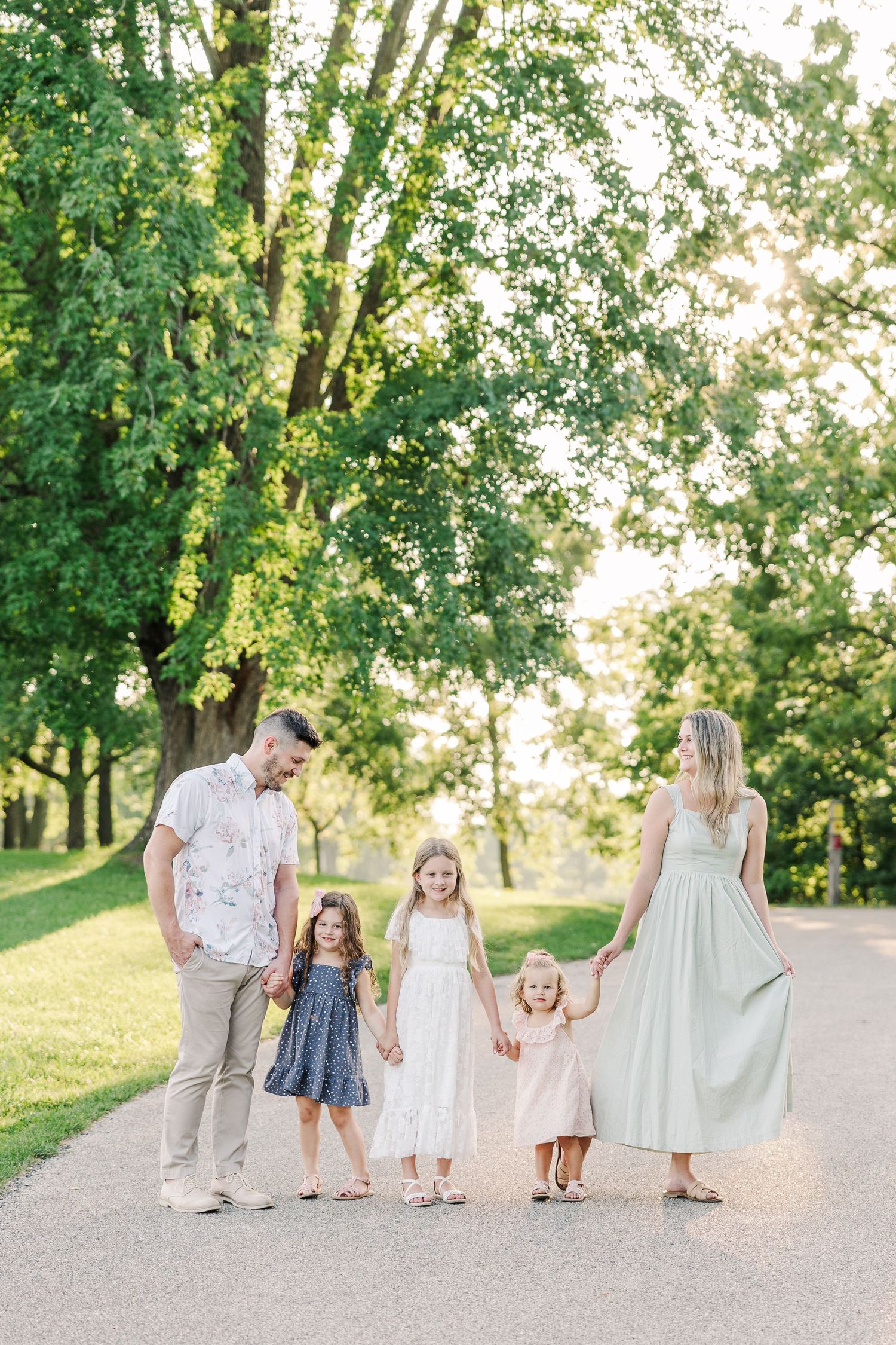 Family walking together on a tree-lined path in summer wearing coordinated pastel outfits.