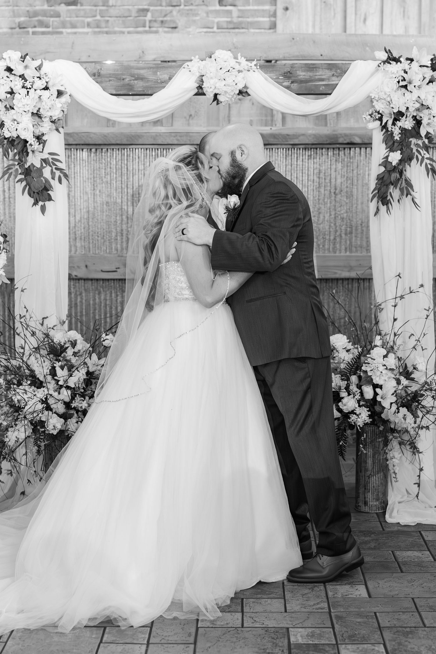 A romantic wedding portrait in black and white against a decorated ceremony backdrop with white draping.