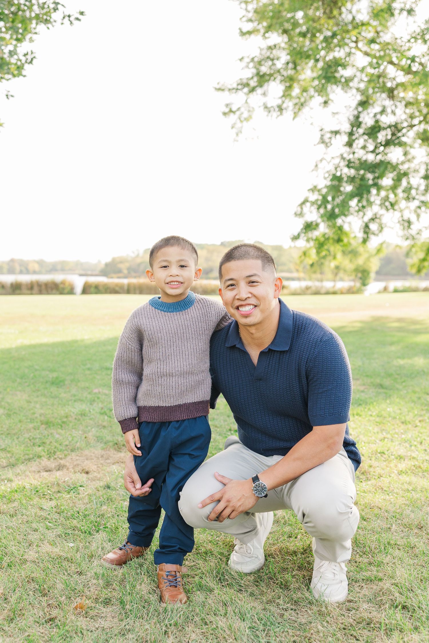 Two people crouching together on grassy lawn during outdoor autumn photo session. Busse Woods
