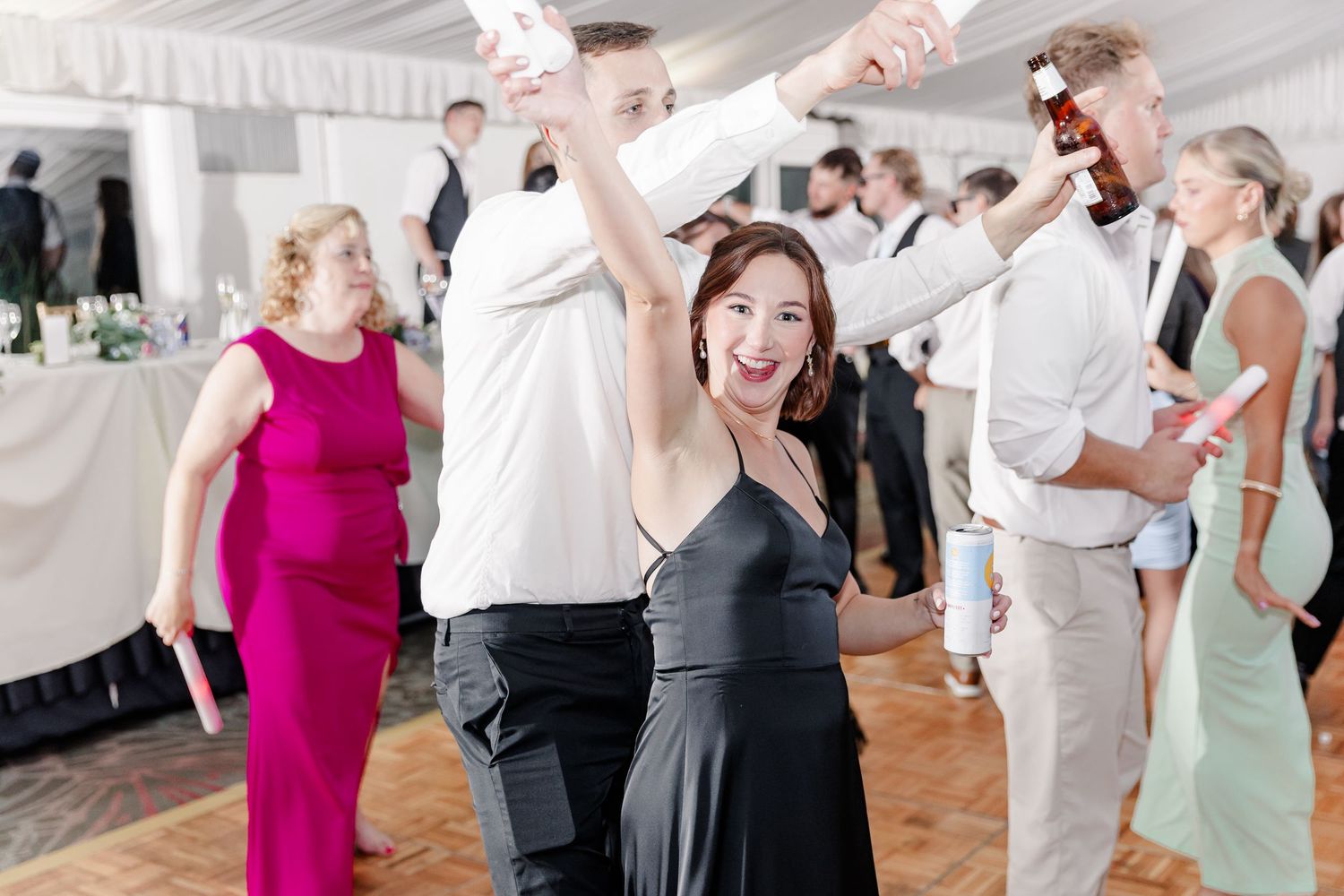 Joyful wedding guest in black dress dancing and raising her arm at lively indoor reception celebration.