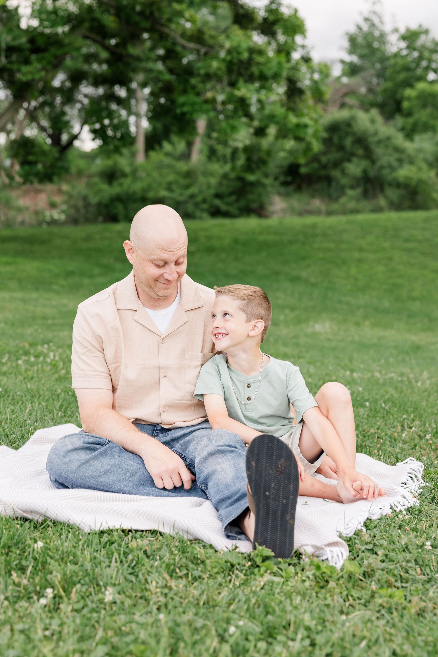 Dad cuddling his son on a blanket during a sweet family photo session at Shamrock Hills Park.