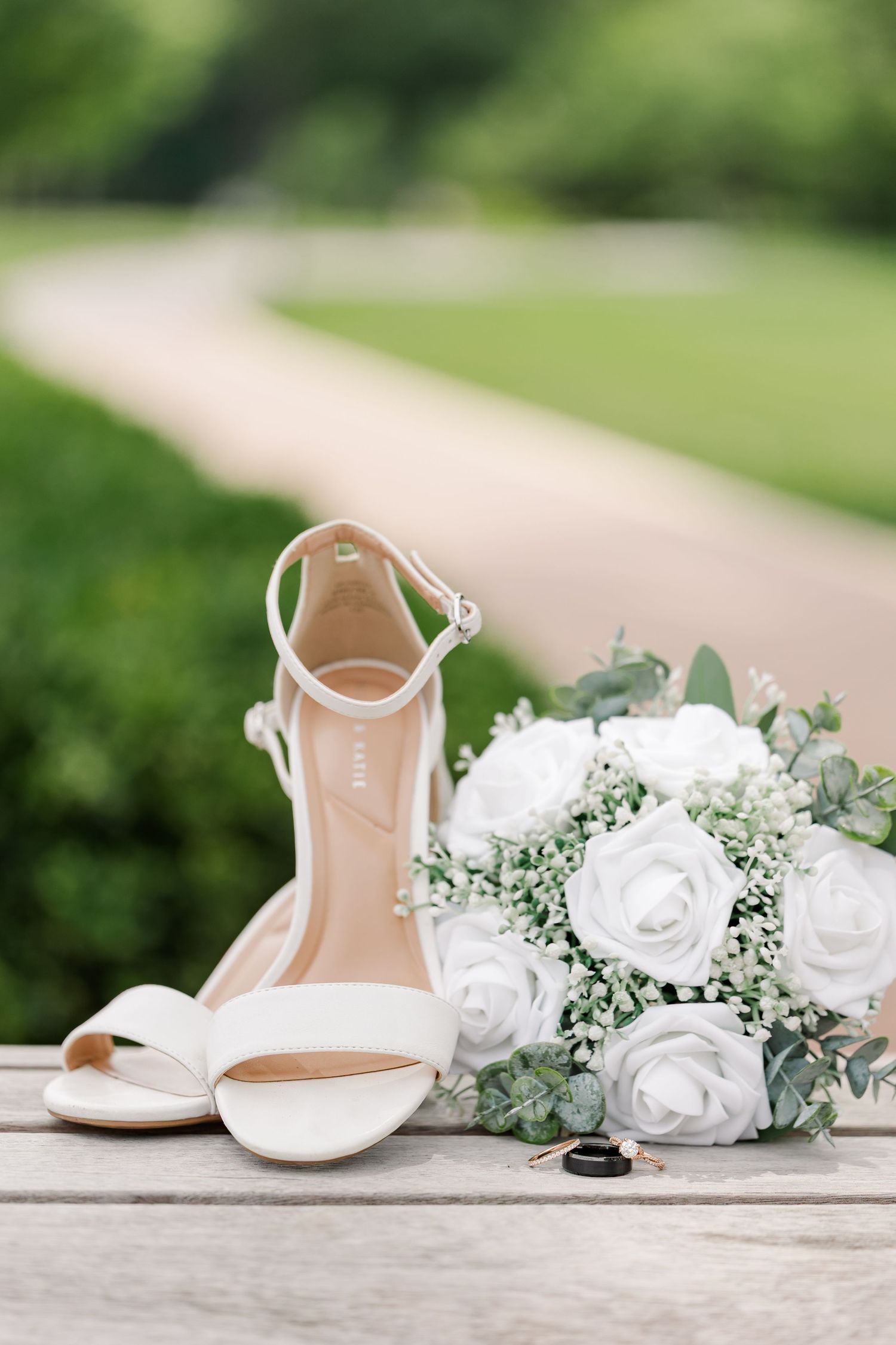 Ivory bridal shoes, white rose bouquet, and wedding rings arranged on a wooden bench at Cantigny Park.