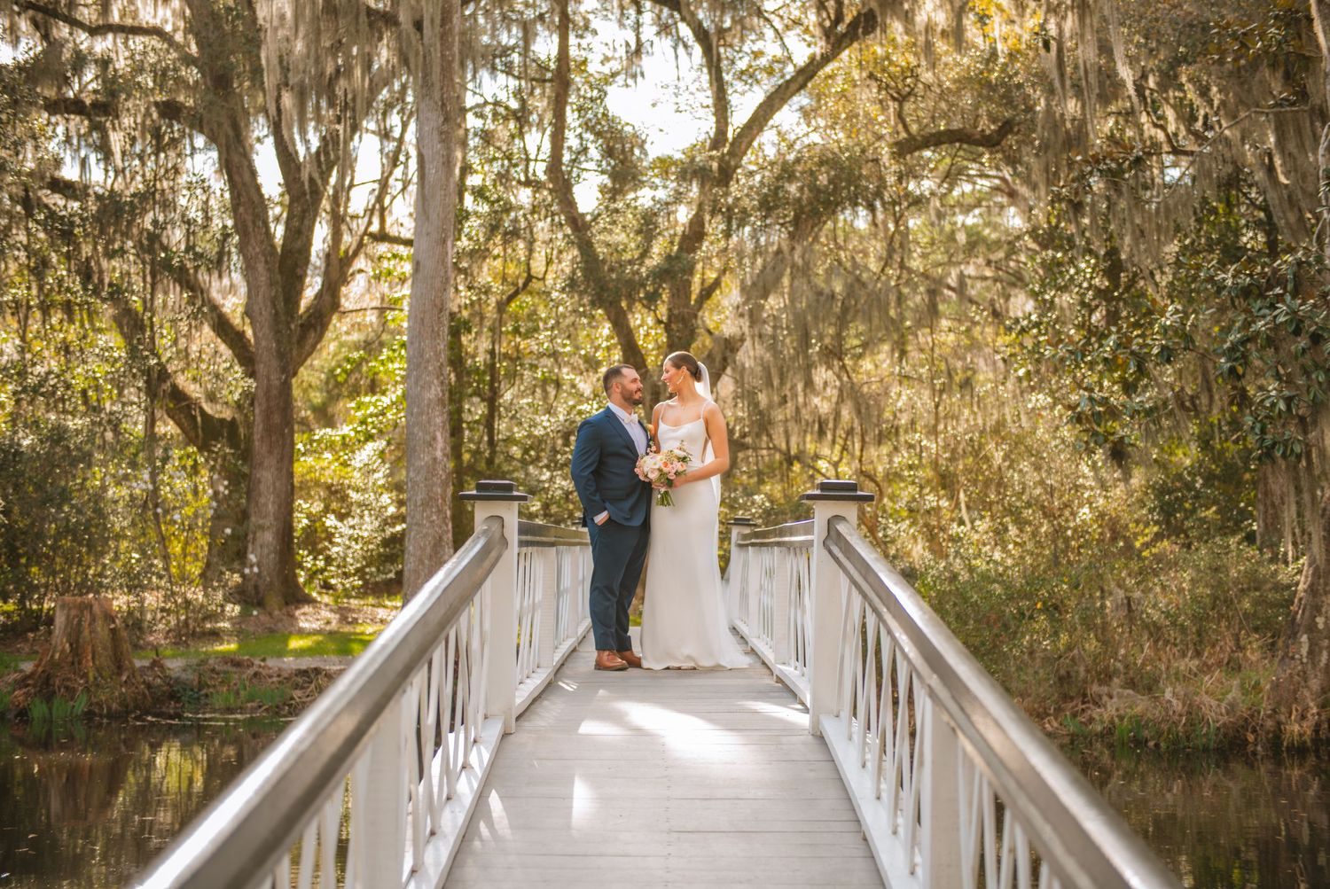 Bride and groom embracing under large trees during a natural outdoor wedding moment. Magnolia Plantation and Gardens