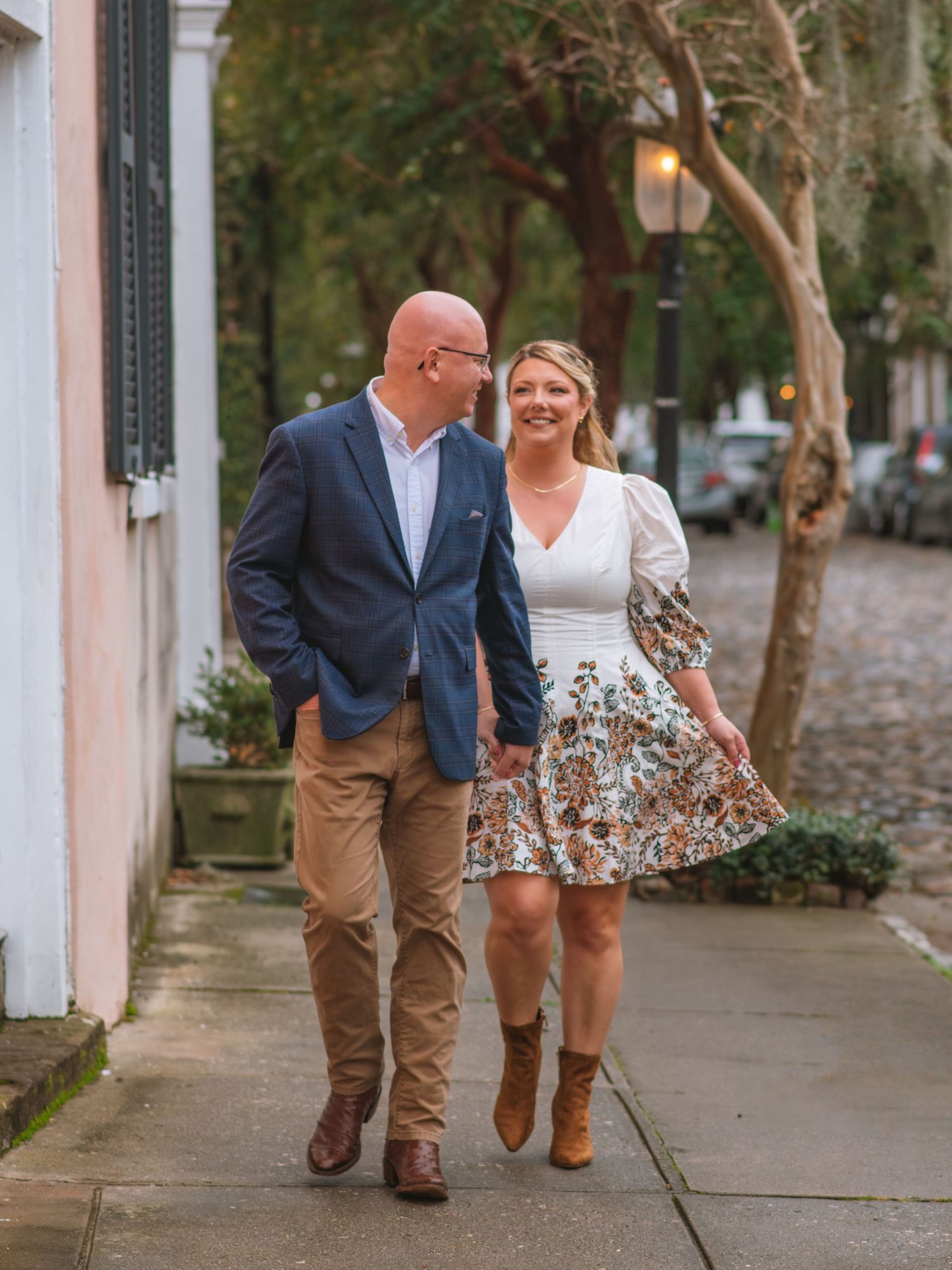 Couple walking hand in hand down a charming street during a relaxed engagement session. Chalmers Street Charleston SC