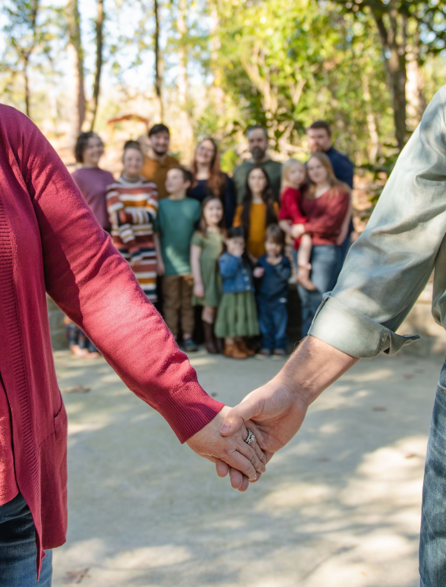 Couple holding hands in foreground with large family gathered behind during an outdoor family session.