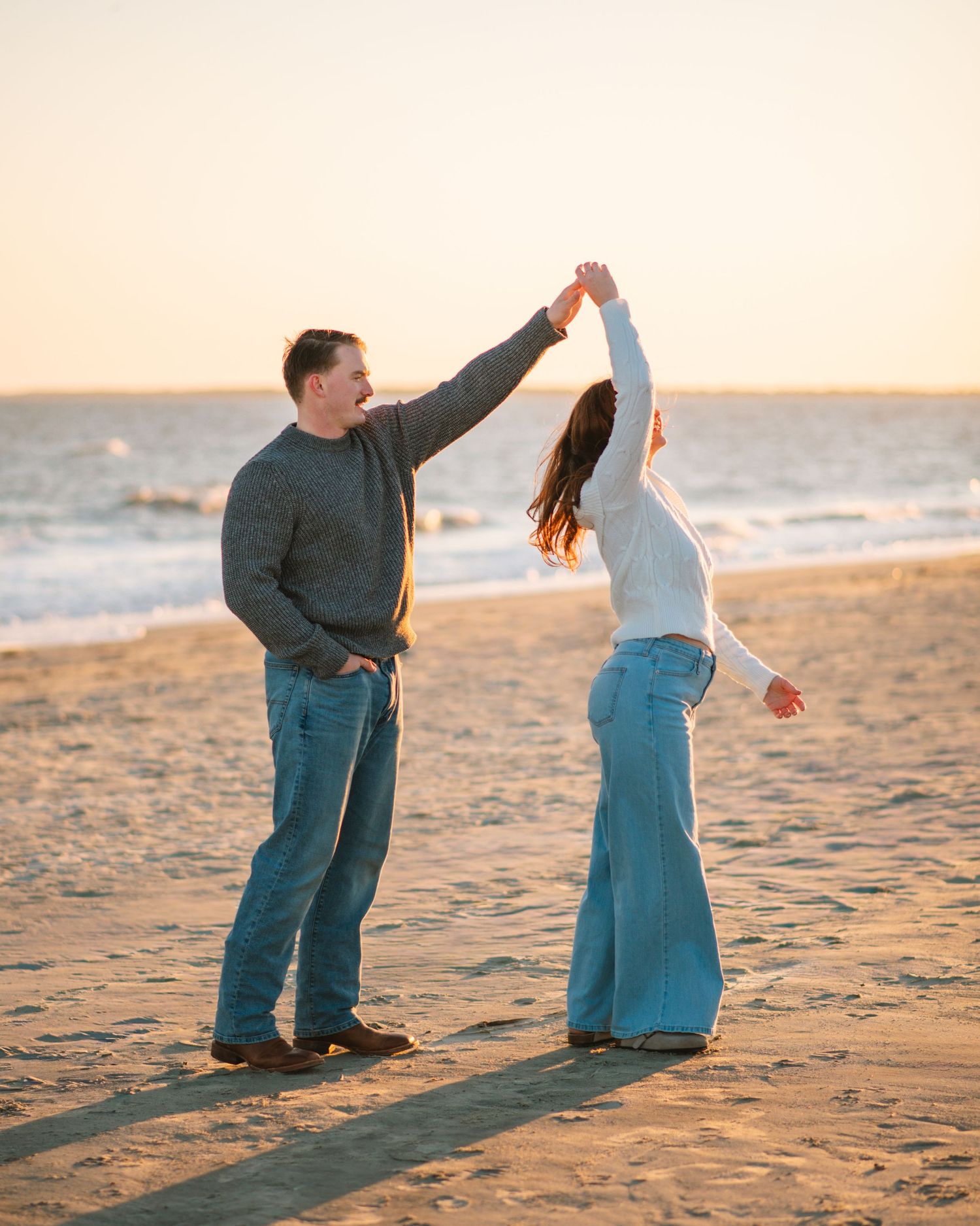 Couple dancing together on the beach during a playful sunset engagement session. on Sullivans Island, Charleston SC