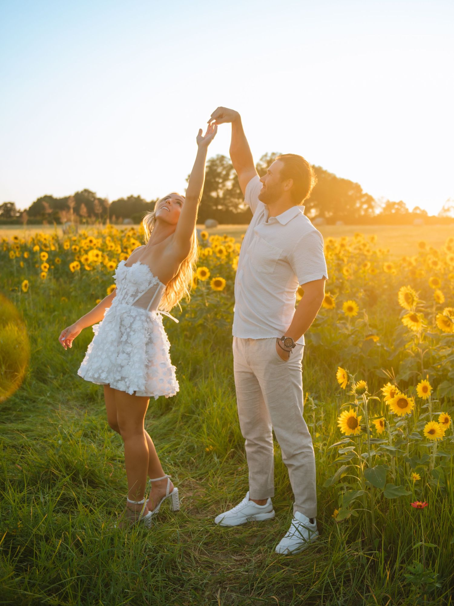 Couple twirling in a sunflower field during a playful and romantic sunset session.