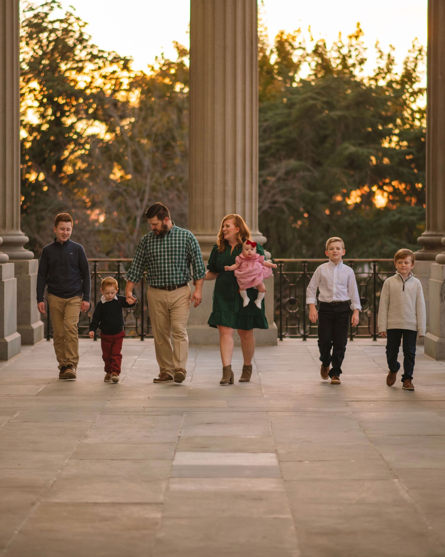 Family walking together between tall columns at sunset during a warm outdoor family session at the South Carolina State House