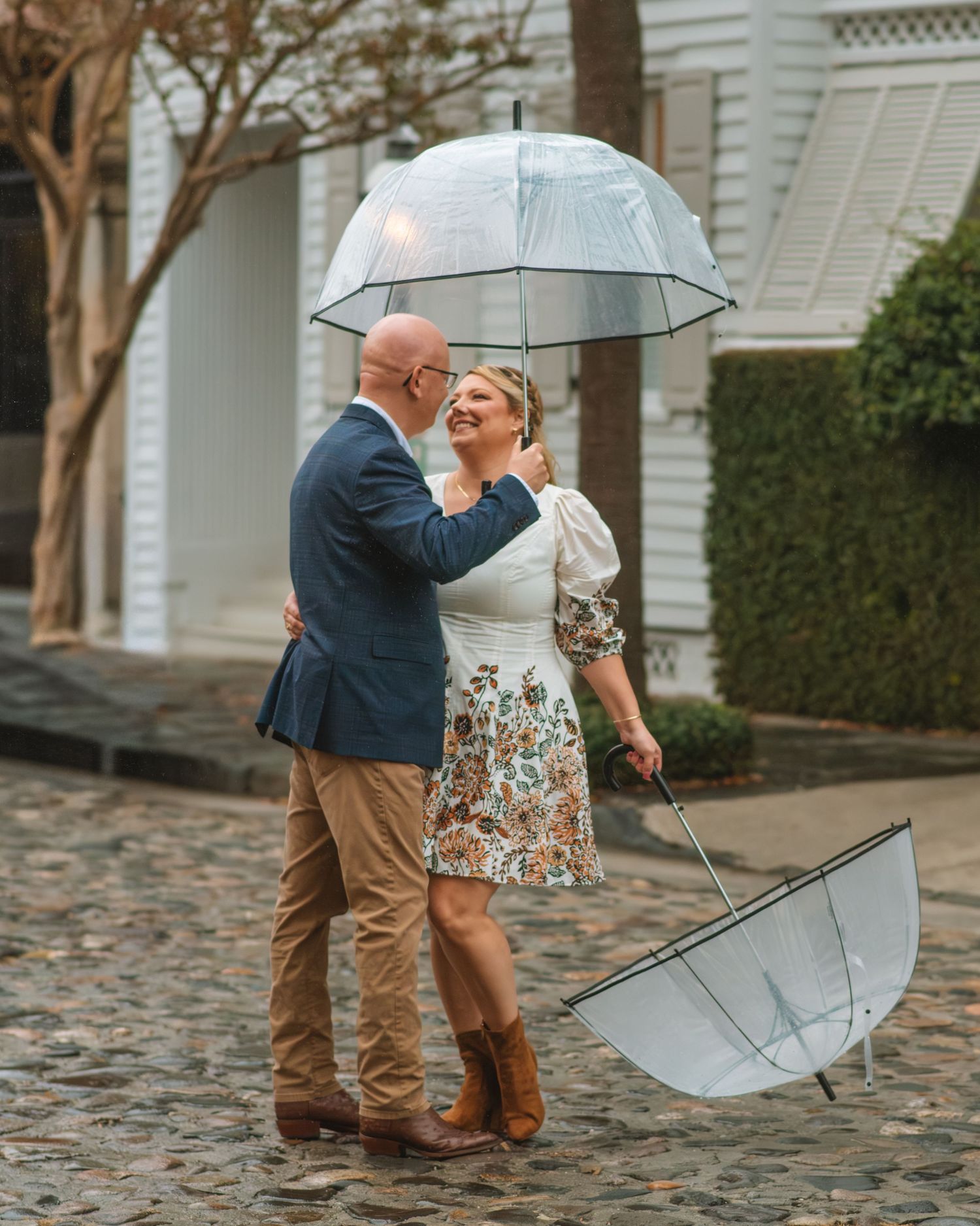 Couple kissing under clear umbrella during a romantic rainy day session Chalmers Street Charleston SC
