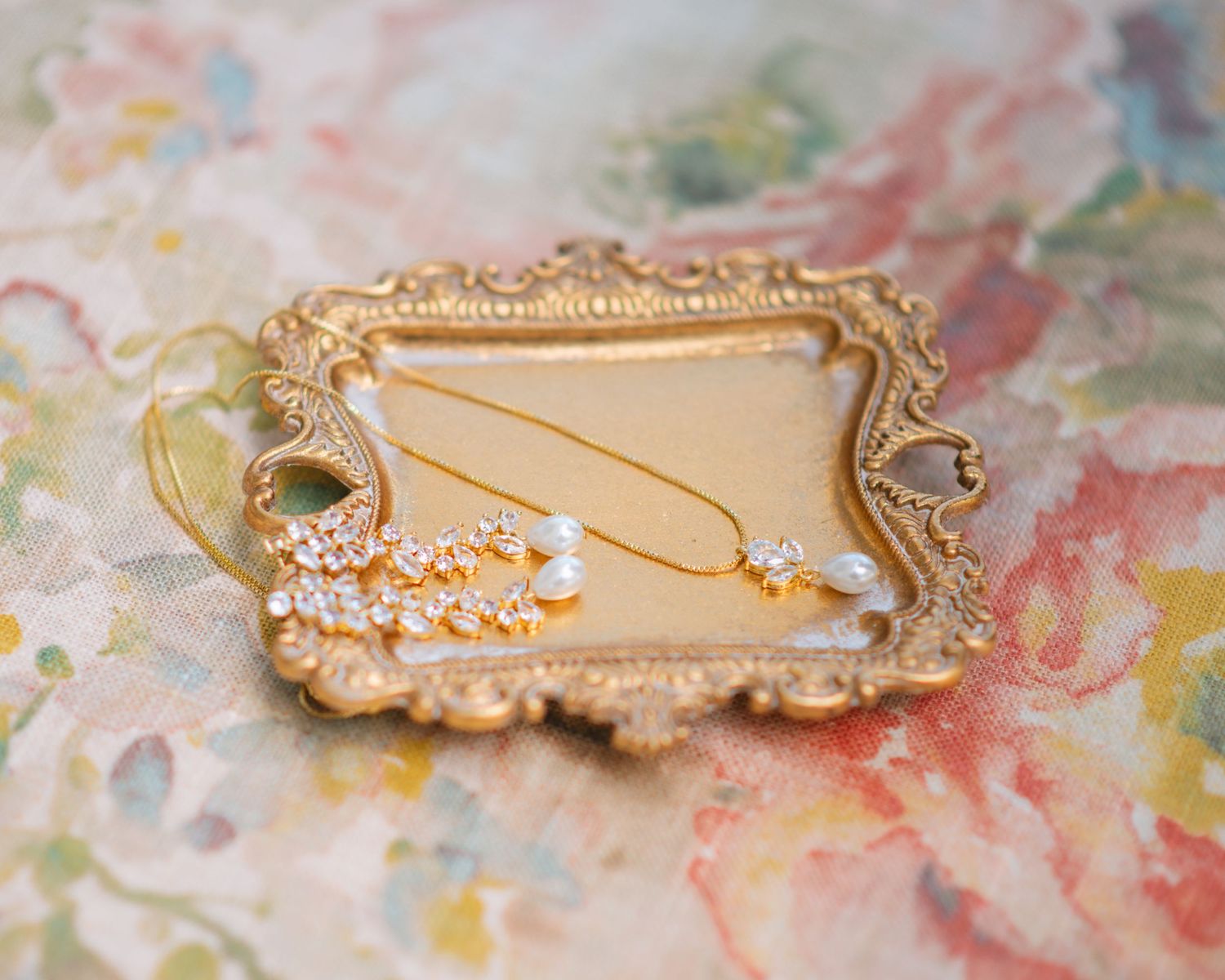 Delicate necklace and jewelry styled on a vintage tray for wedding detail photography.