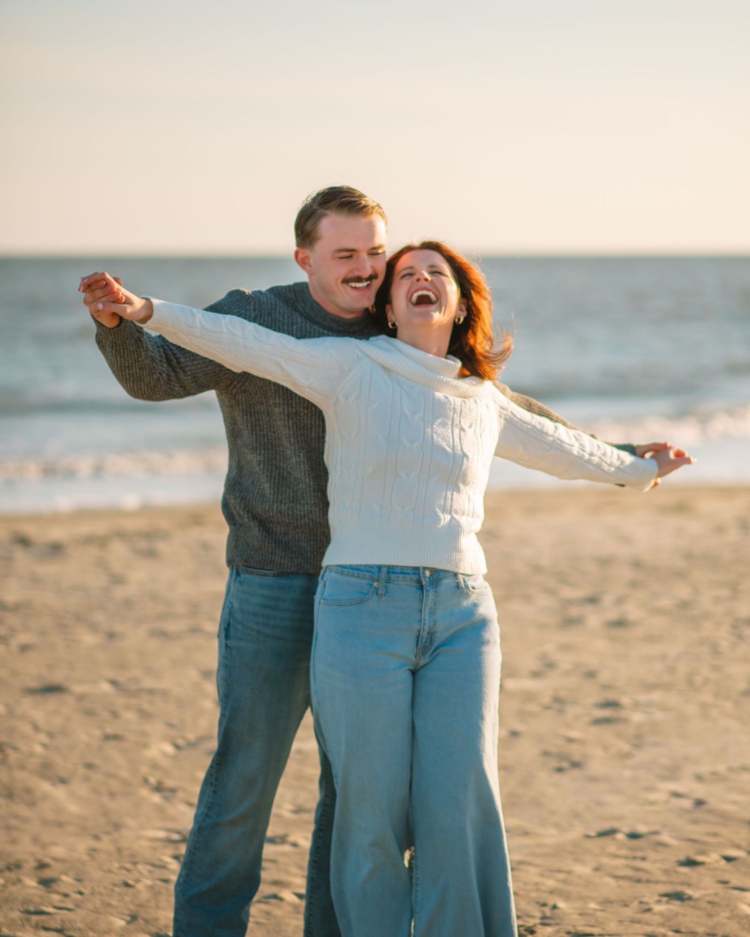 Couple laughing with arms outstretched during a joyful beach session at sunset. on Sullivans Island, Charleston SC