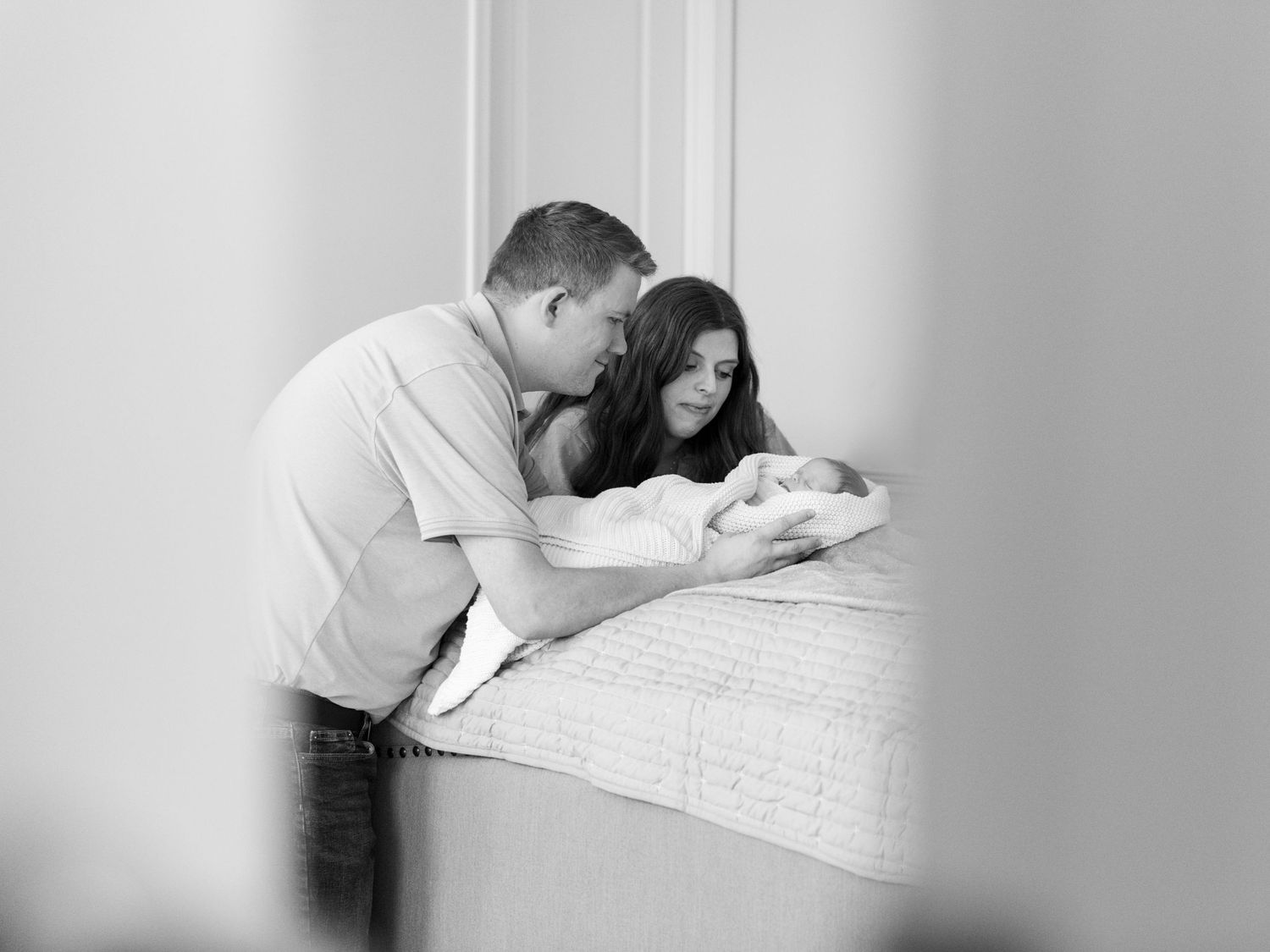 Parents leaning over newborn baby during a soft and intimate in-home newborn photography session