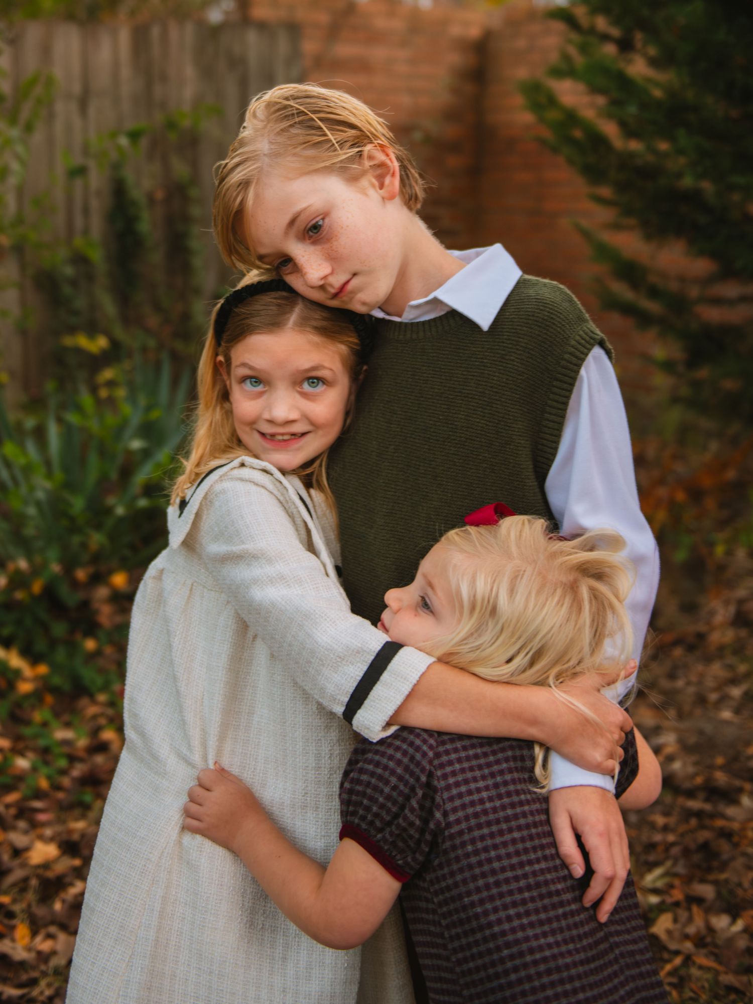 Older siblings hugging younger sibling during a sweet candid moment in a fall family session.