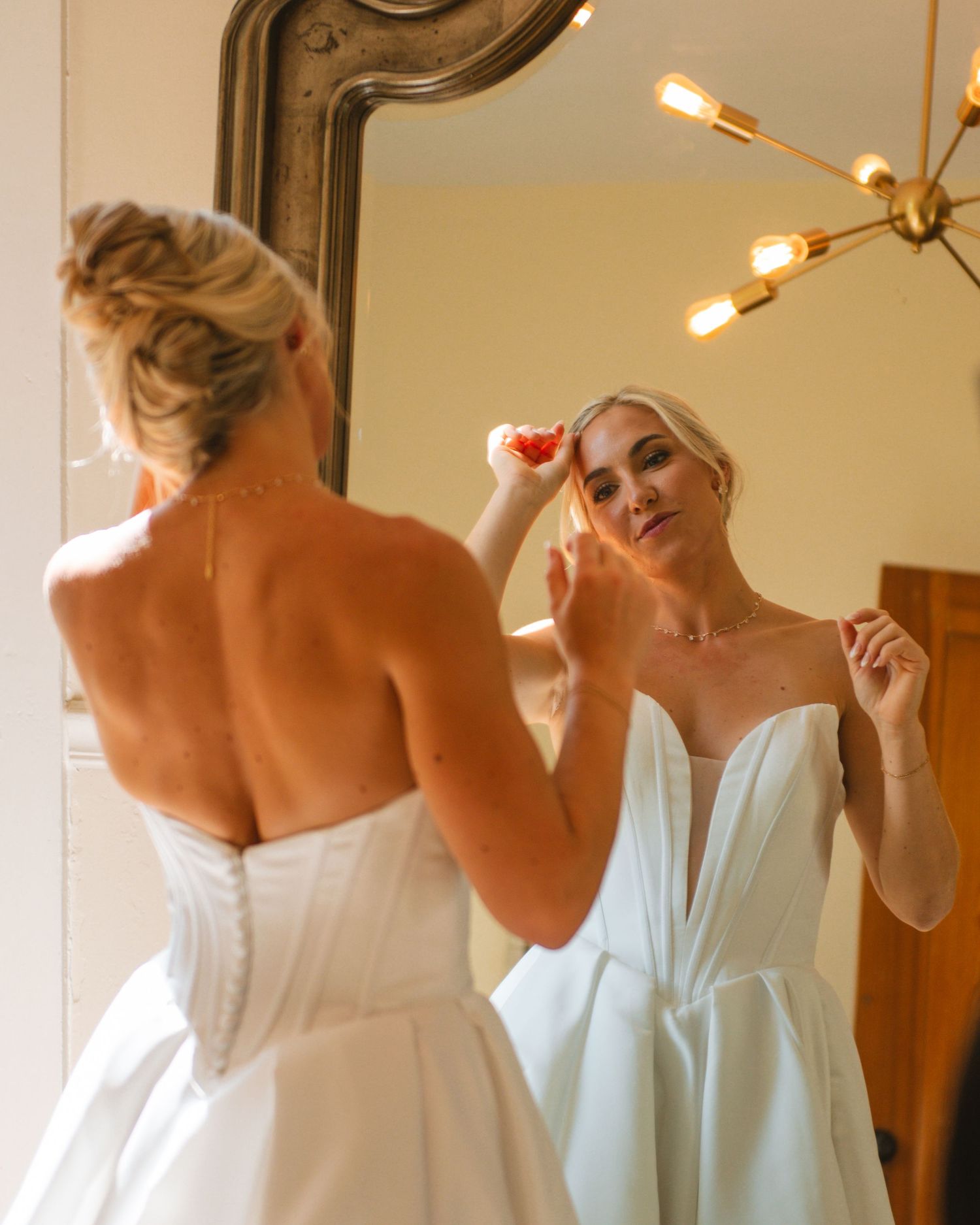 Bride applying makeup in mirror during getting ready moments before wedding ceremony.