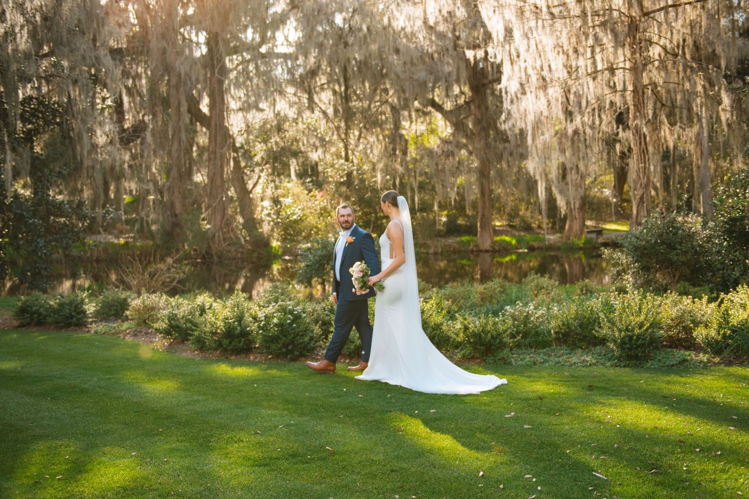 Bride and groom walking through moss-covered trees during a romantic outdoor wedding portrait in South Carolina.