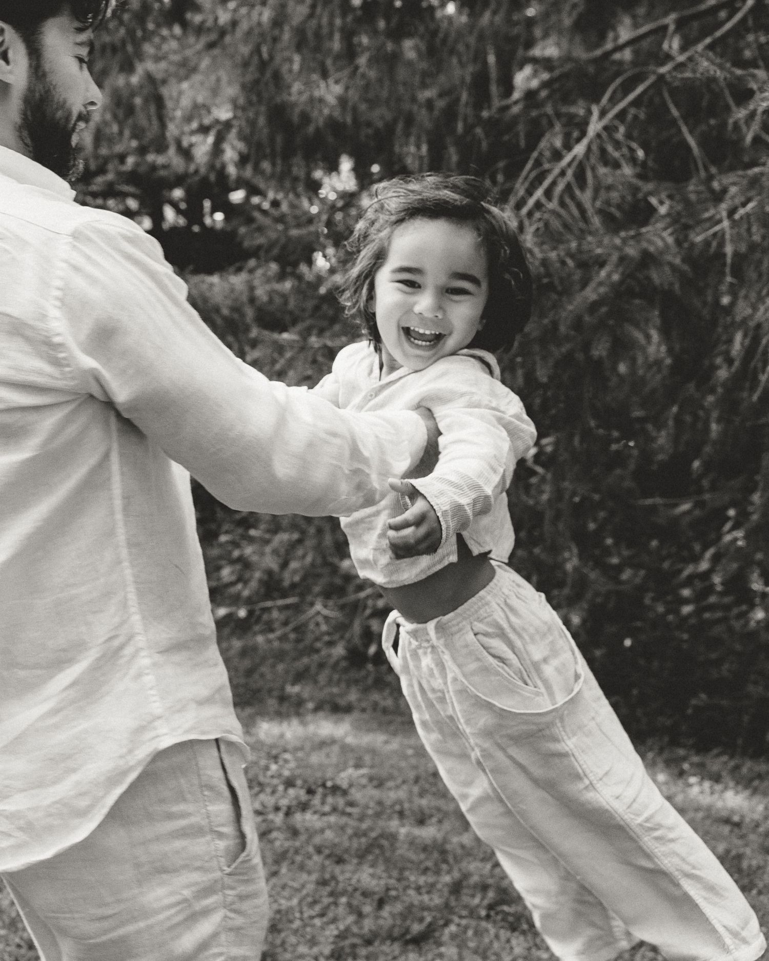 Father swinging his smiling young son during a candid outdoor family photography session in Woodbridge, Connecticut.