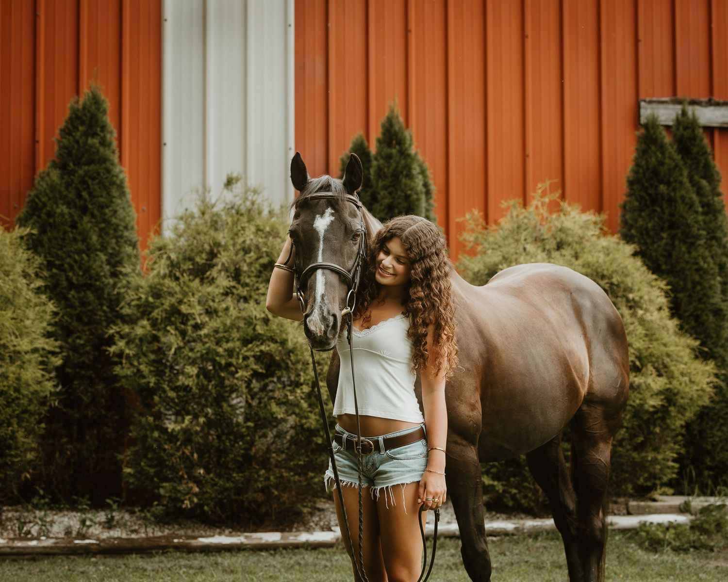 Young equestrian standing with her horse beside a red barn during a Connecticut portrait session.